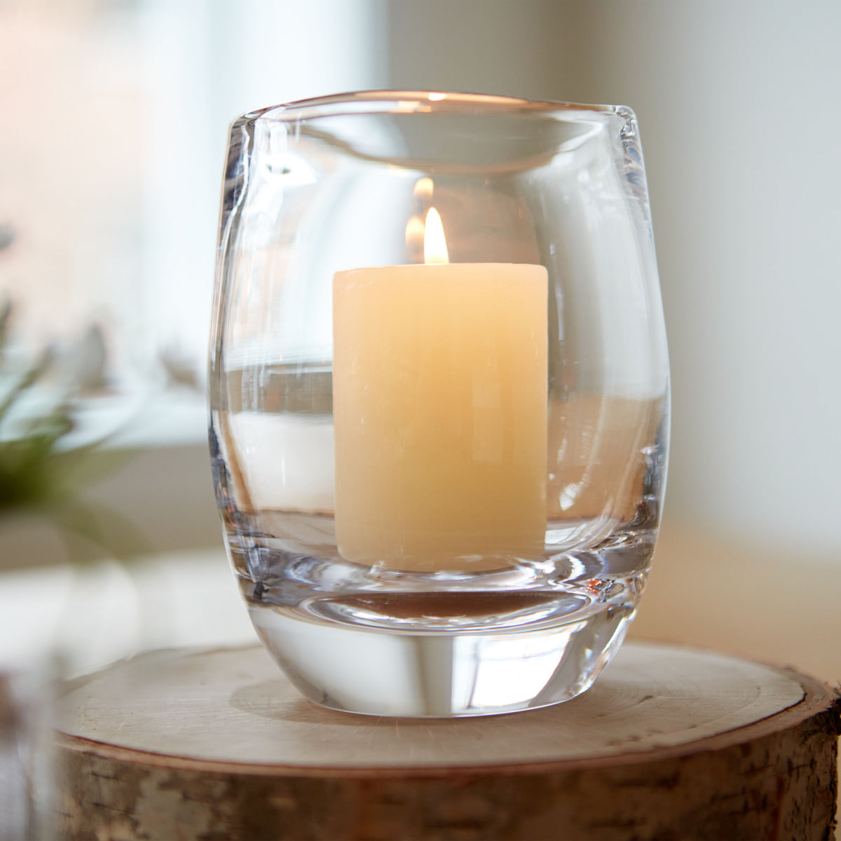 Cream-colored pillar candle inside clear glass hurricane holder on wooden base.