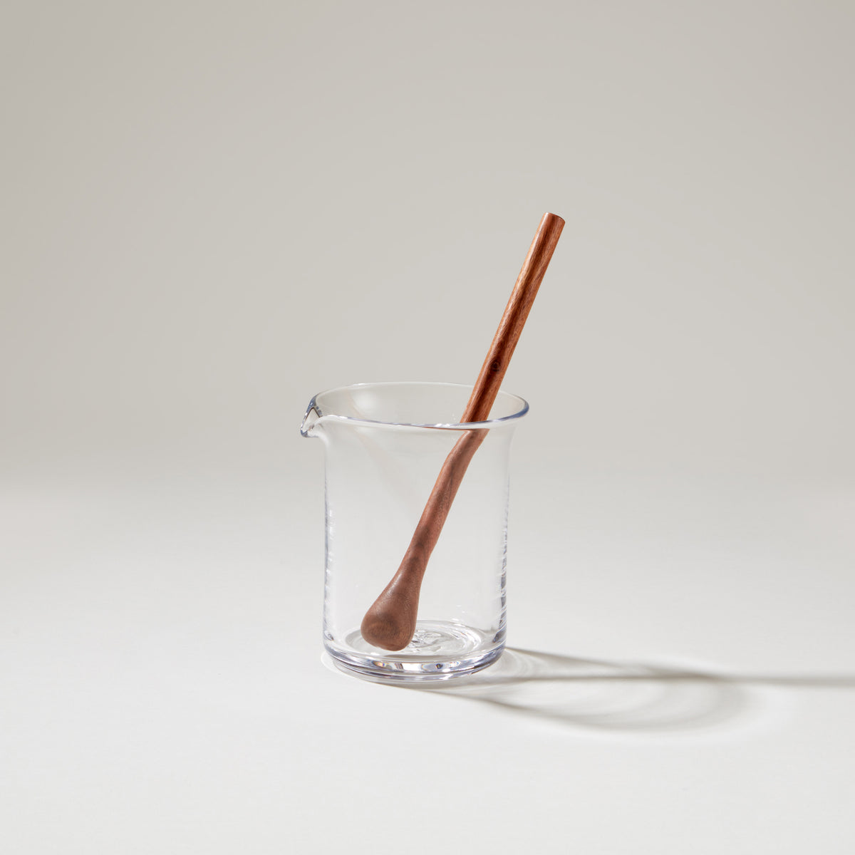Brown wooden cocktail stirrer with rounded handle resting in a clear glass mixing pitcher filled with water.