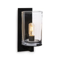 Black wall sconce with clear cylindrical glass shade and lit Edison-style filament bulb inside.