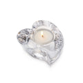 Clear glass heart-shaped tealight holder with lit white candle inside.