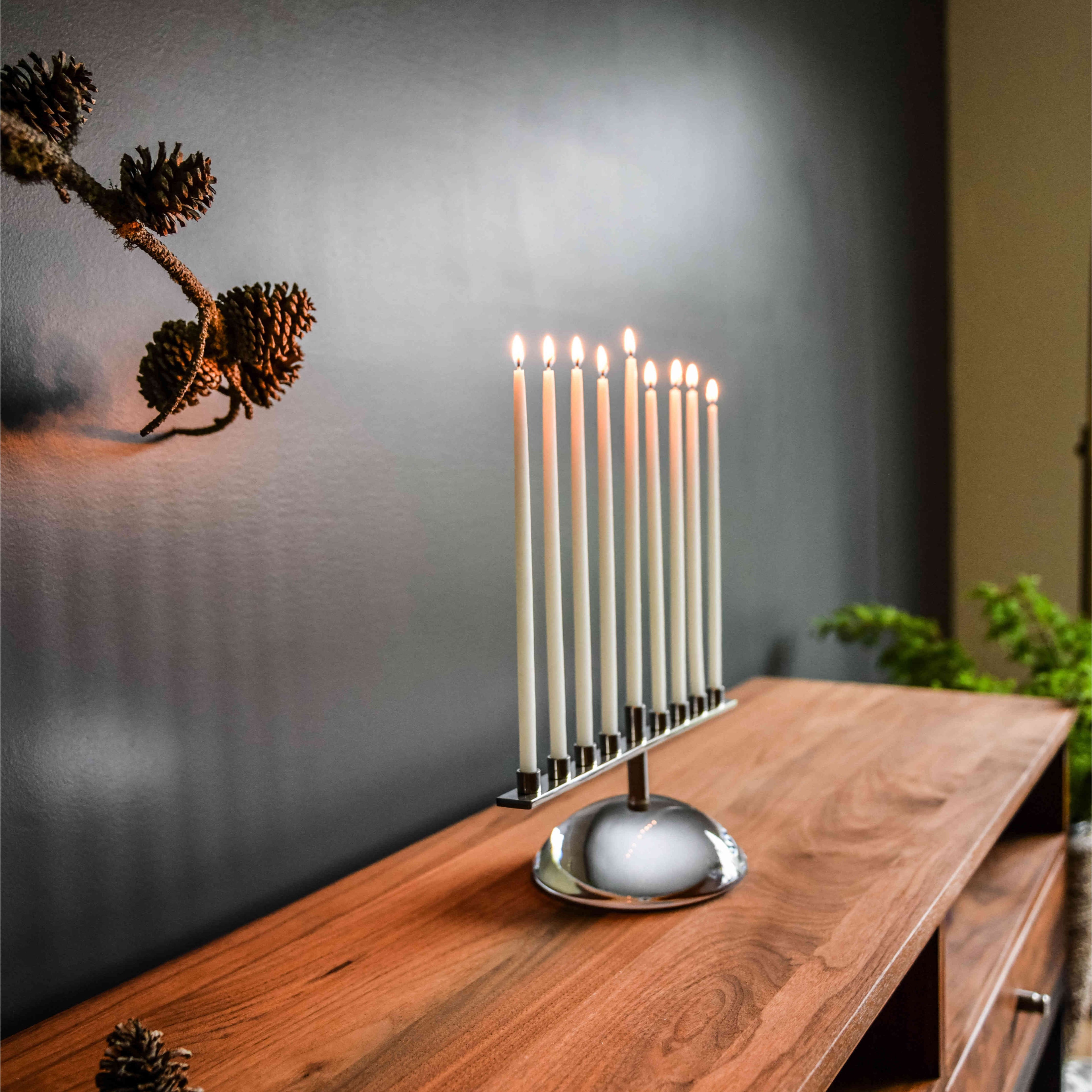 Menorah with nine lit white candles in a polished metal base on a wooden table.