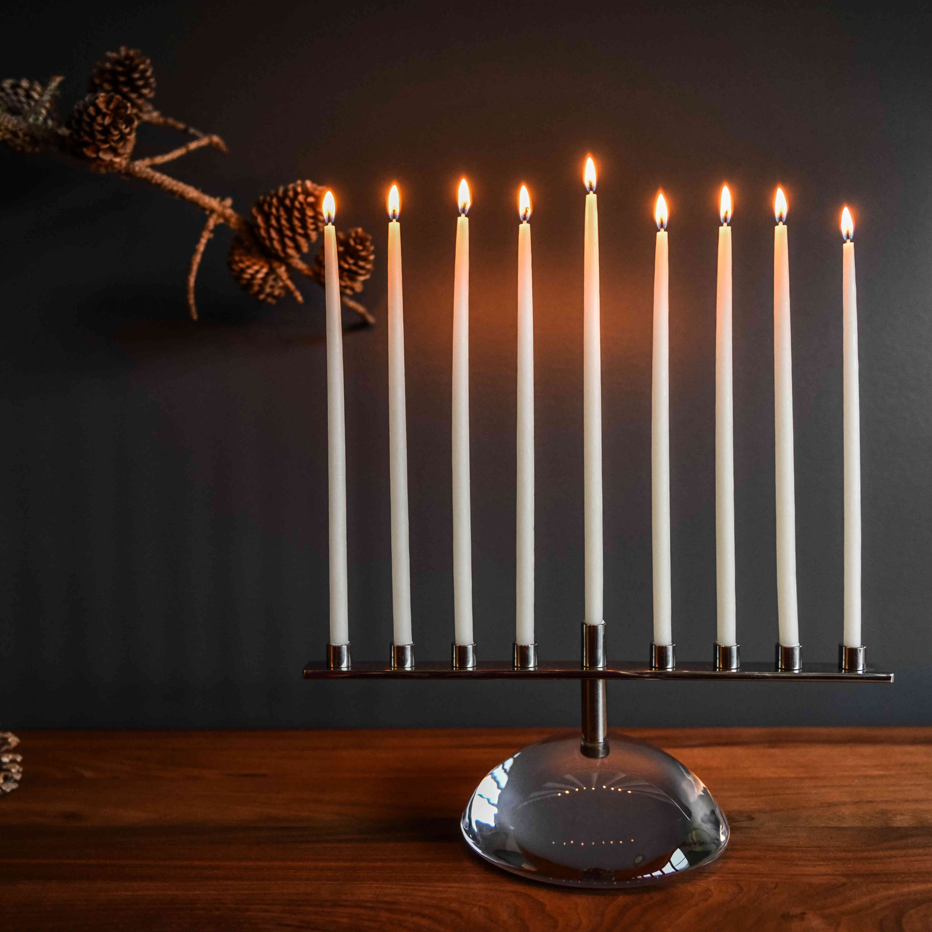 Nine-branch menorah with lit white candles in metal holders on a rounded stone base.
