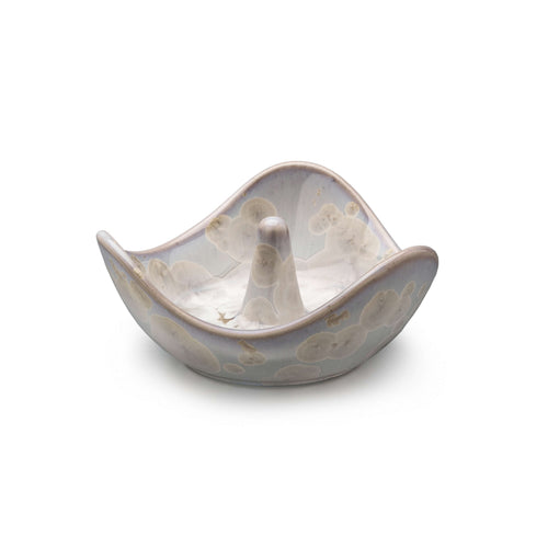 Cream-colored ceramic ring holder with wavy edges and a central cone post, featuring subtle etched details.