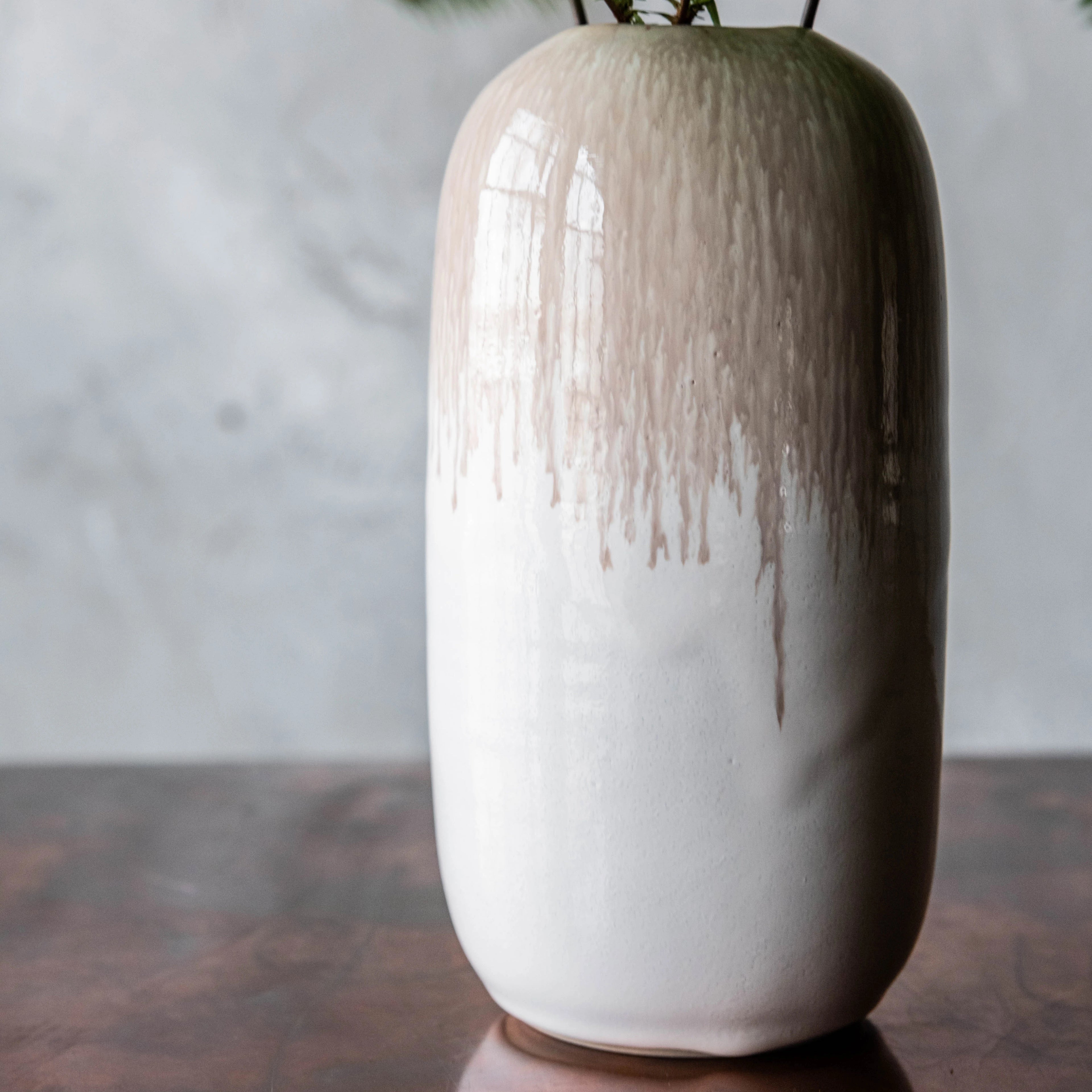 Cylindrical ceramic vase with tapered top, cream glaze transitioning to tan textured finish, holding dried greenery.