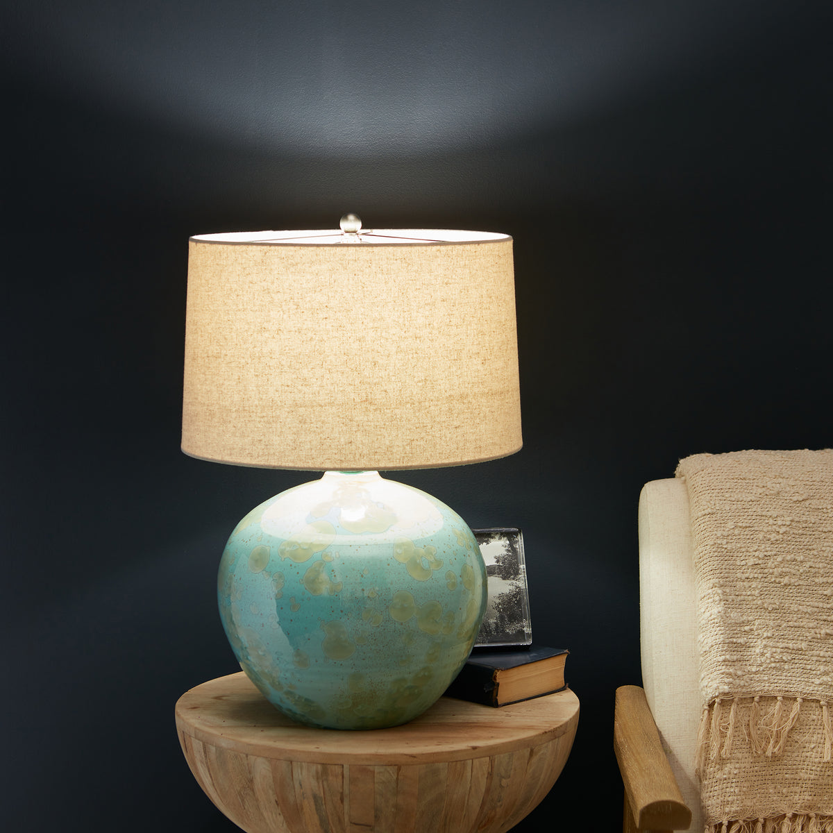 Jade-colored spherical ceramic table lamp with linen drum shade, displayed on wooden side table.