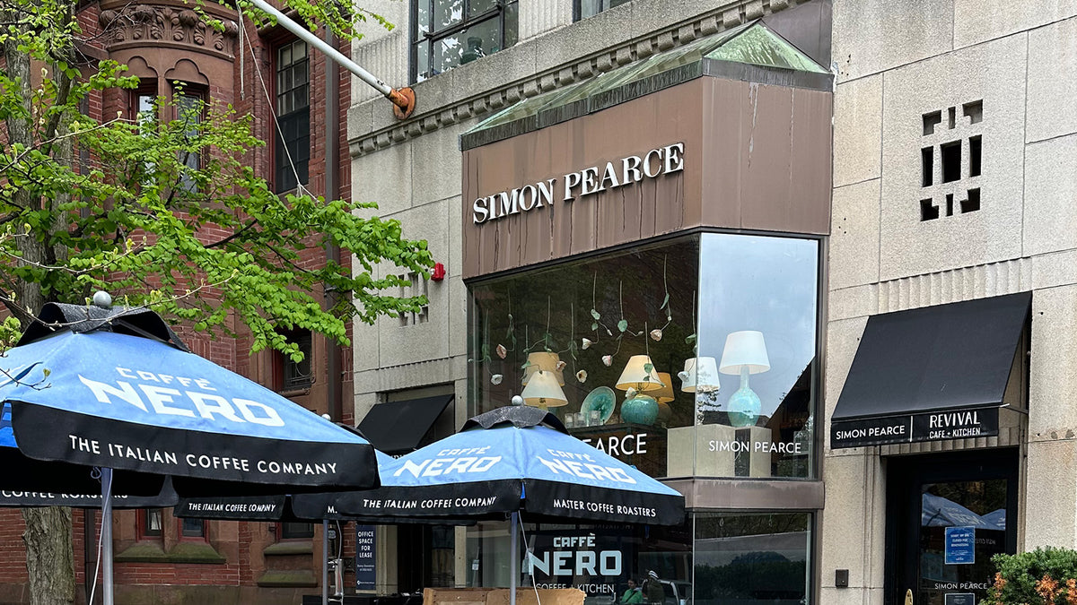 Exterior of the Simon Pearce retail store on Newbury Street in Boston, Massachusetts, a corner building with bronze cladding and large windows displaying lamps and glass pieces