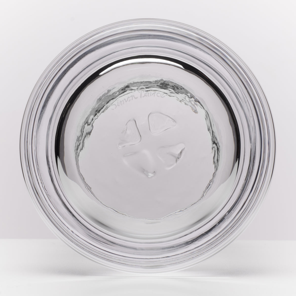 A clear glass with a thick, rounded base and a textured, hammered pattern, shown from the bottom on a light gray background.