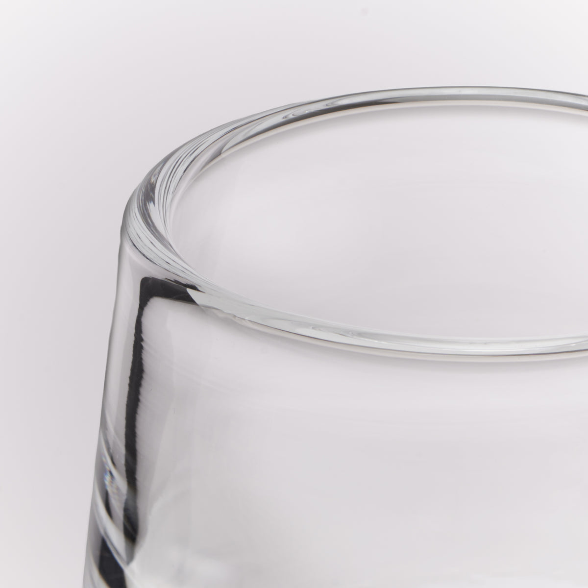 Close-up of a clear glass tumbler showing the thick rim and part of the body against a white background.