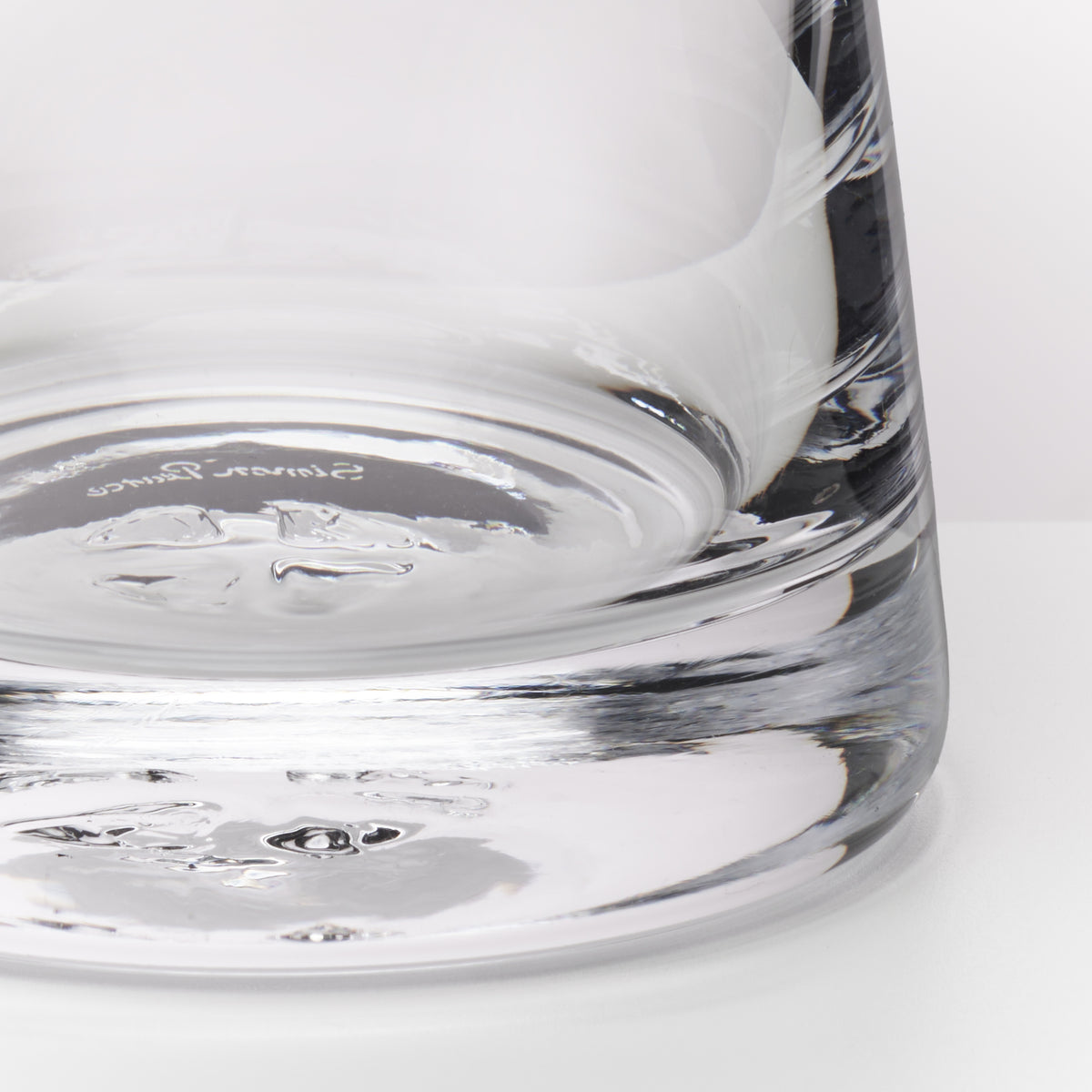 Close-up of a clear glass tumbler showing the thick textured base and a portion of the upper section on a white background.