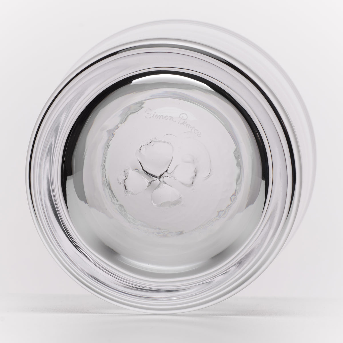 A round, clear glass with a wide, flared rim, photographed from the bottom on a clean white background. The bottom of the glass features a subtle brand logo and a faint 'Simon Pearce' brand signature near the top.