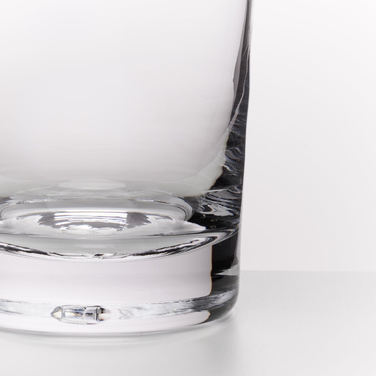 Close-up of a clear glass tumbler with a thick, rounded base on a clean white surface.