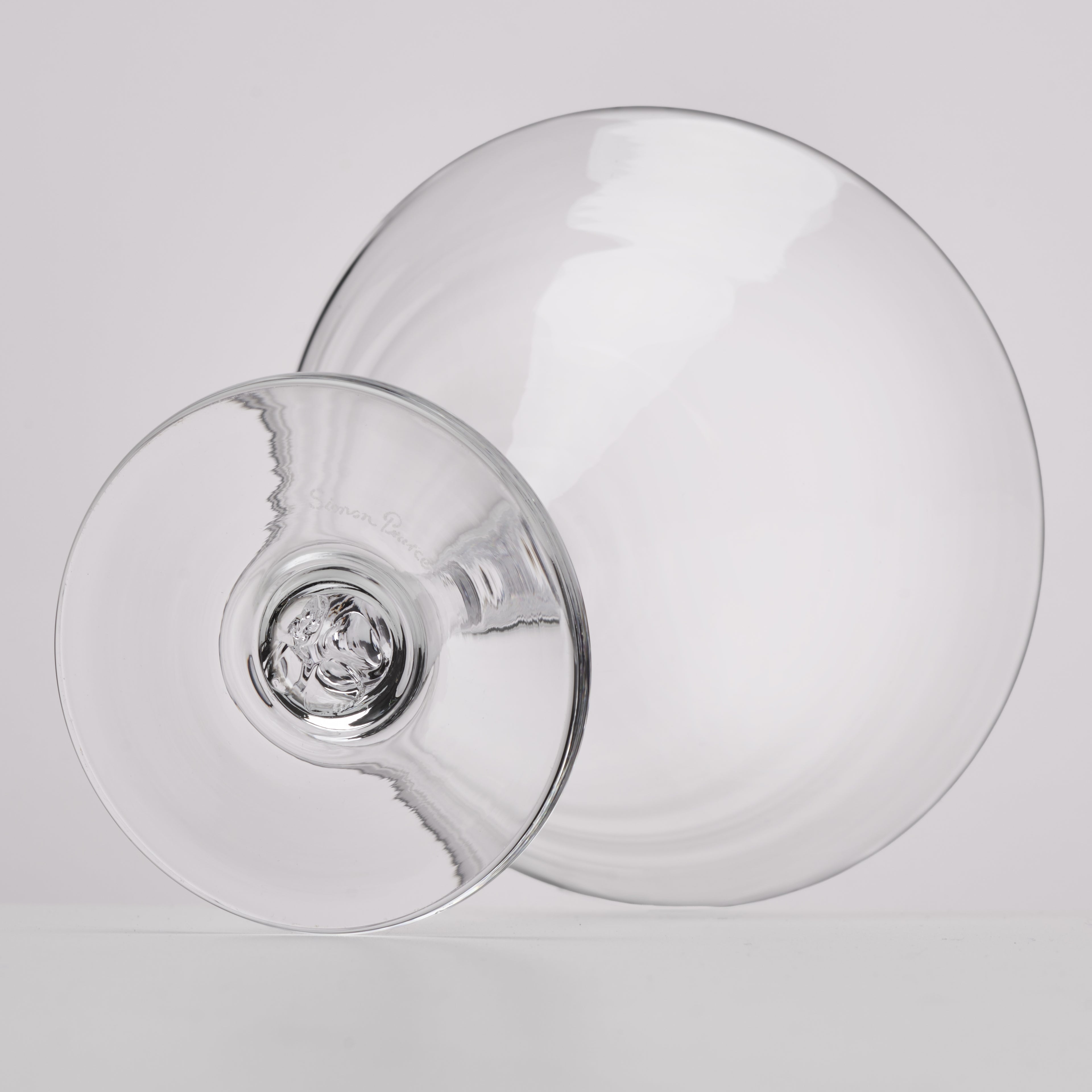 A clear glass stemmed martini glass or cocktail glass shown from an angled top-down view on a light gray studio background.