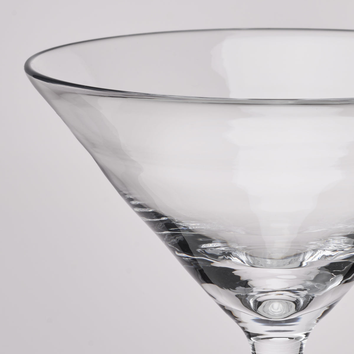 A close-up of a clear glass martini glass on a light gray background.