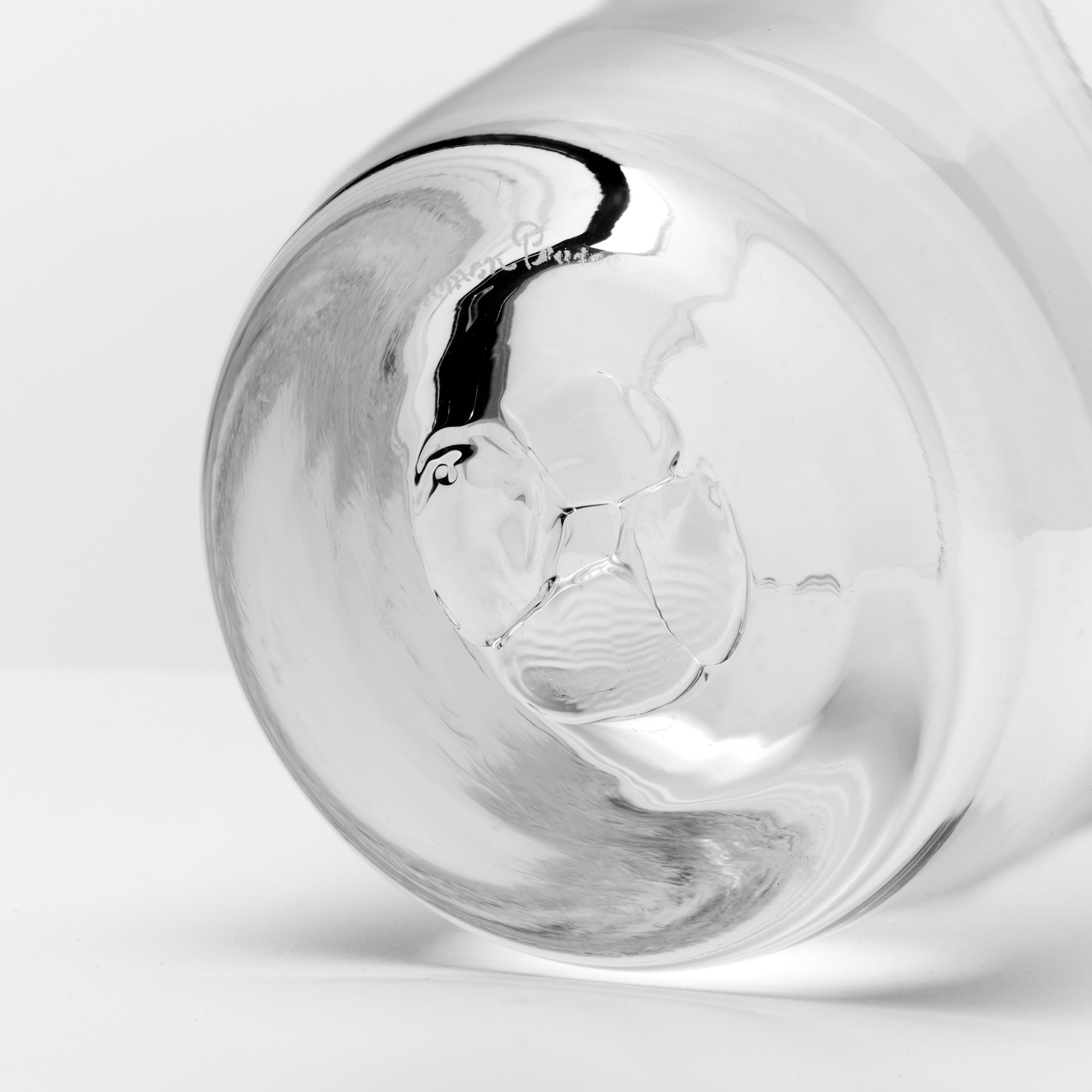 A close-up studio shot of a clear glass tumbler or cup base on a light gray background.