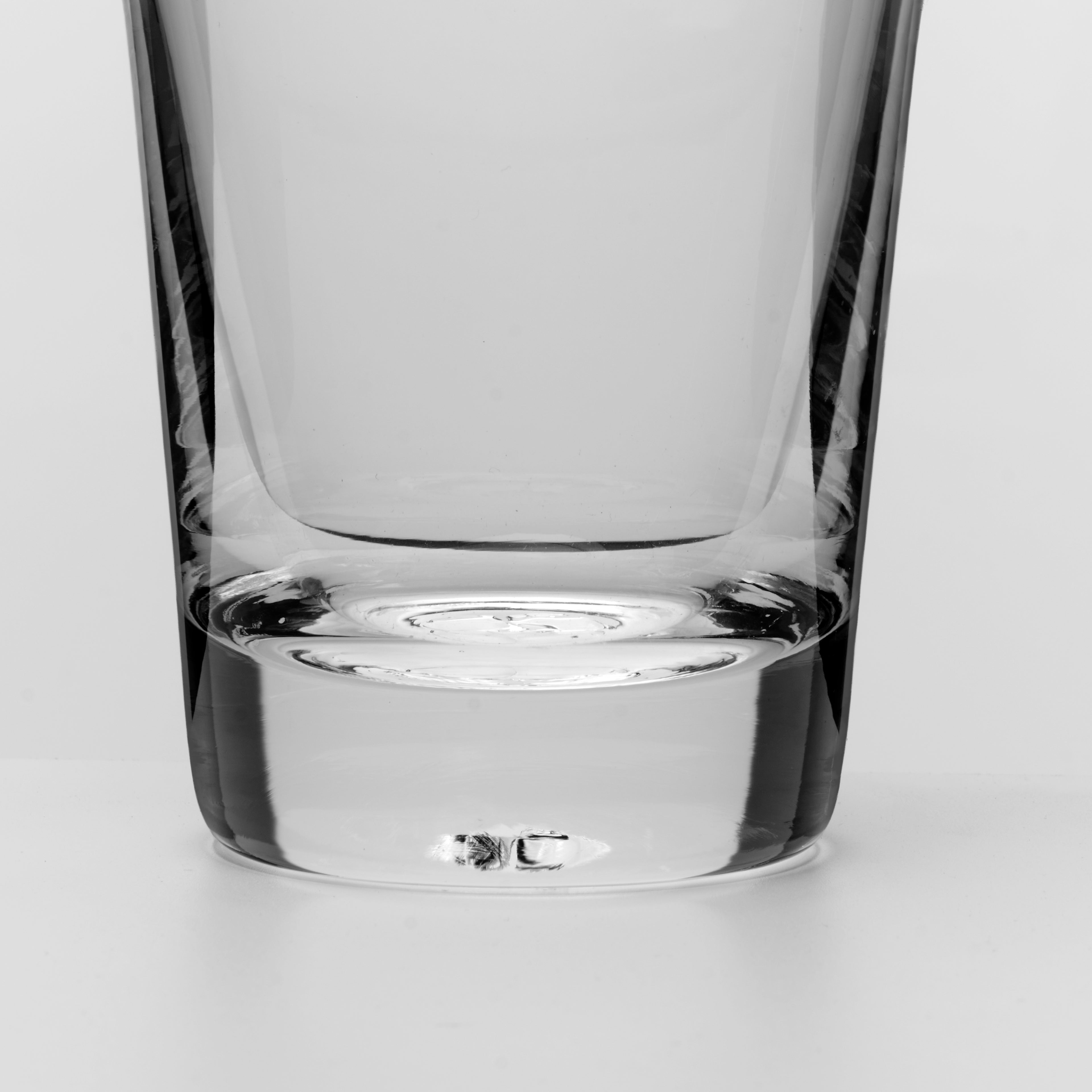 A close-up studio shot of the base and lower half of a clear glass tumbler on a light gray background.