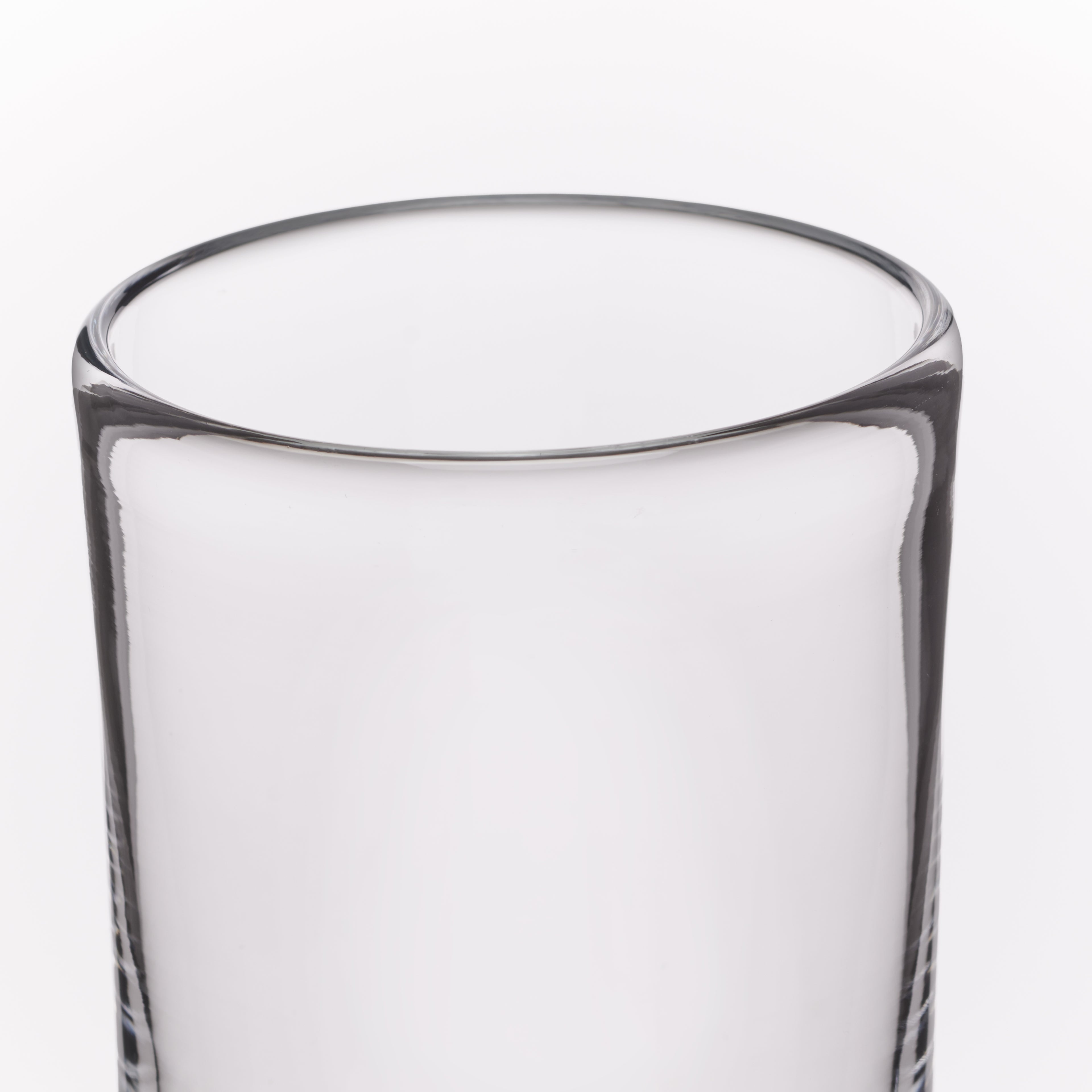 A close-up of a clear glass tumbler with a thick, rounded rim and subtle vertical textured detailing near the base, shown against a plain white background.