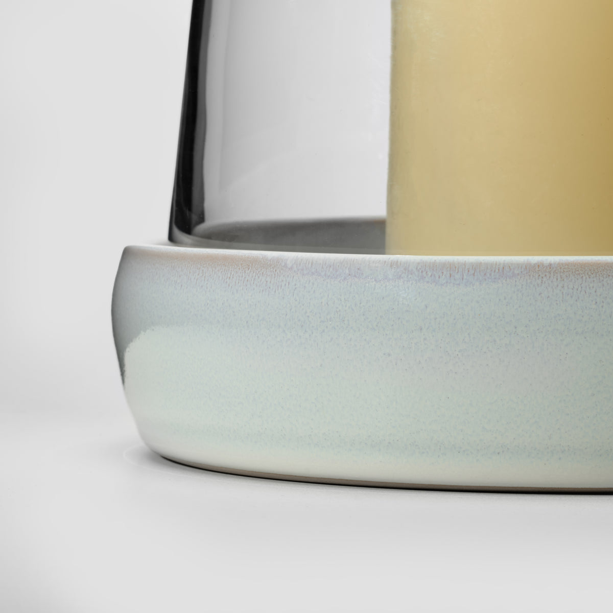 Tall hurricane candle with cream ceramic base and pale yellow wax center, shown at close angle.