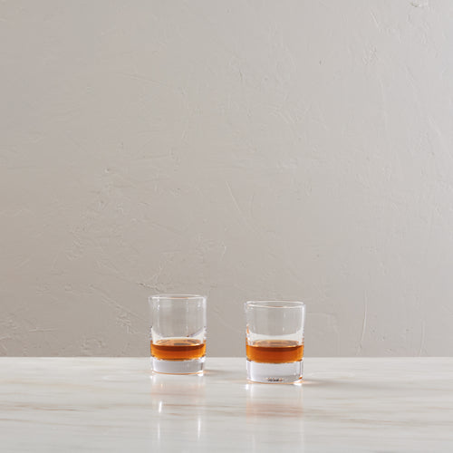 Two clear whiskey glasses filled with amber liquid, placed side by side on a white surface.