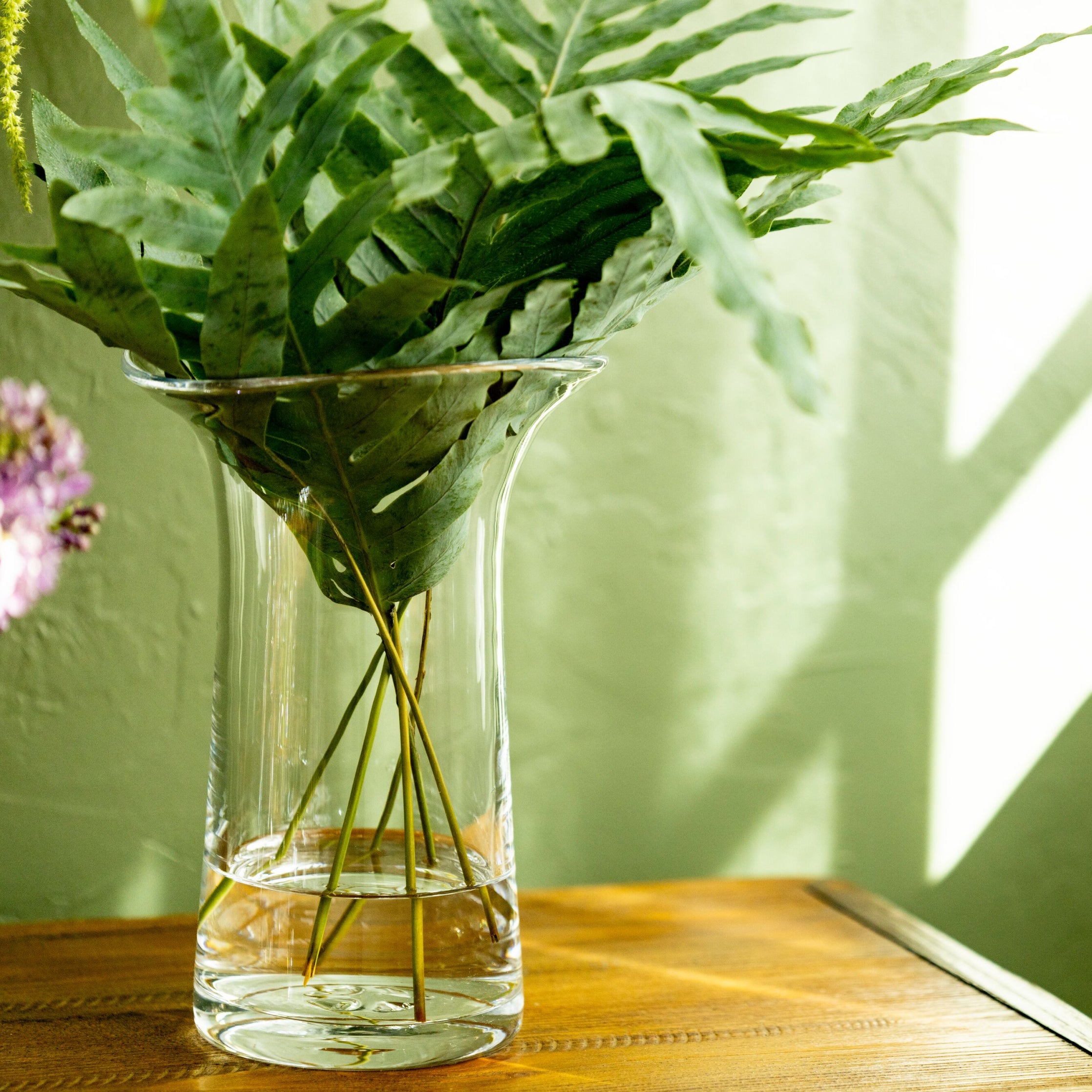 Clear glass cylindrical vase with vertical ridges holding green foliage and pink flowers in water.