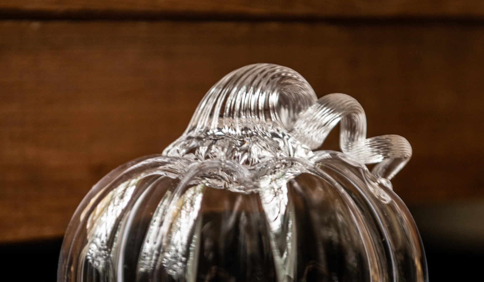 Close-up detail of the stem and twisted vine of a Simon Pearce handblown clear glass pumpkin sculpture against a dark wood background