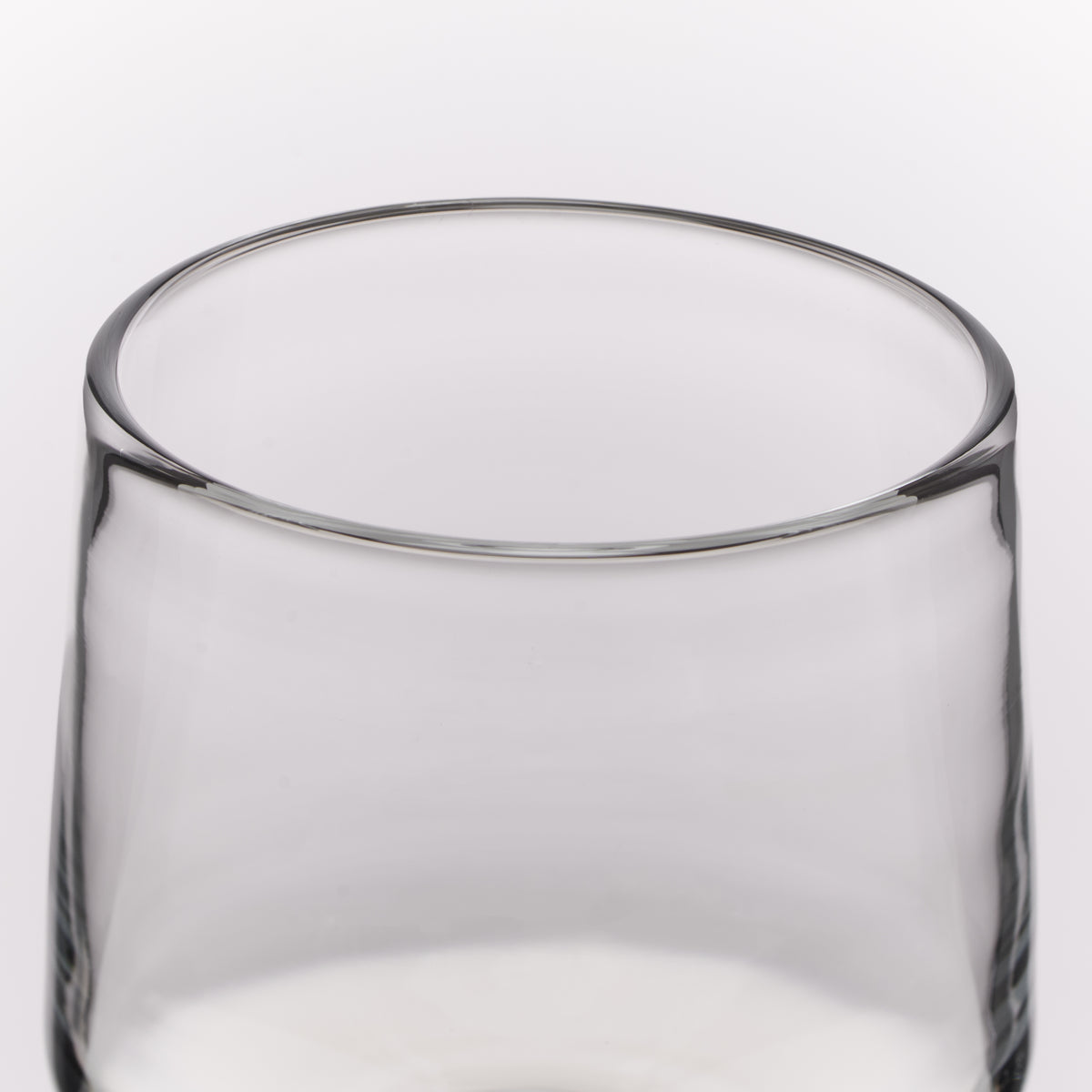 A close-up of a clear glass tumbler with a thick rim, shown against a plain white background.