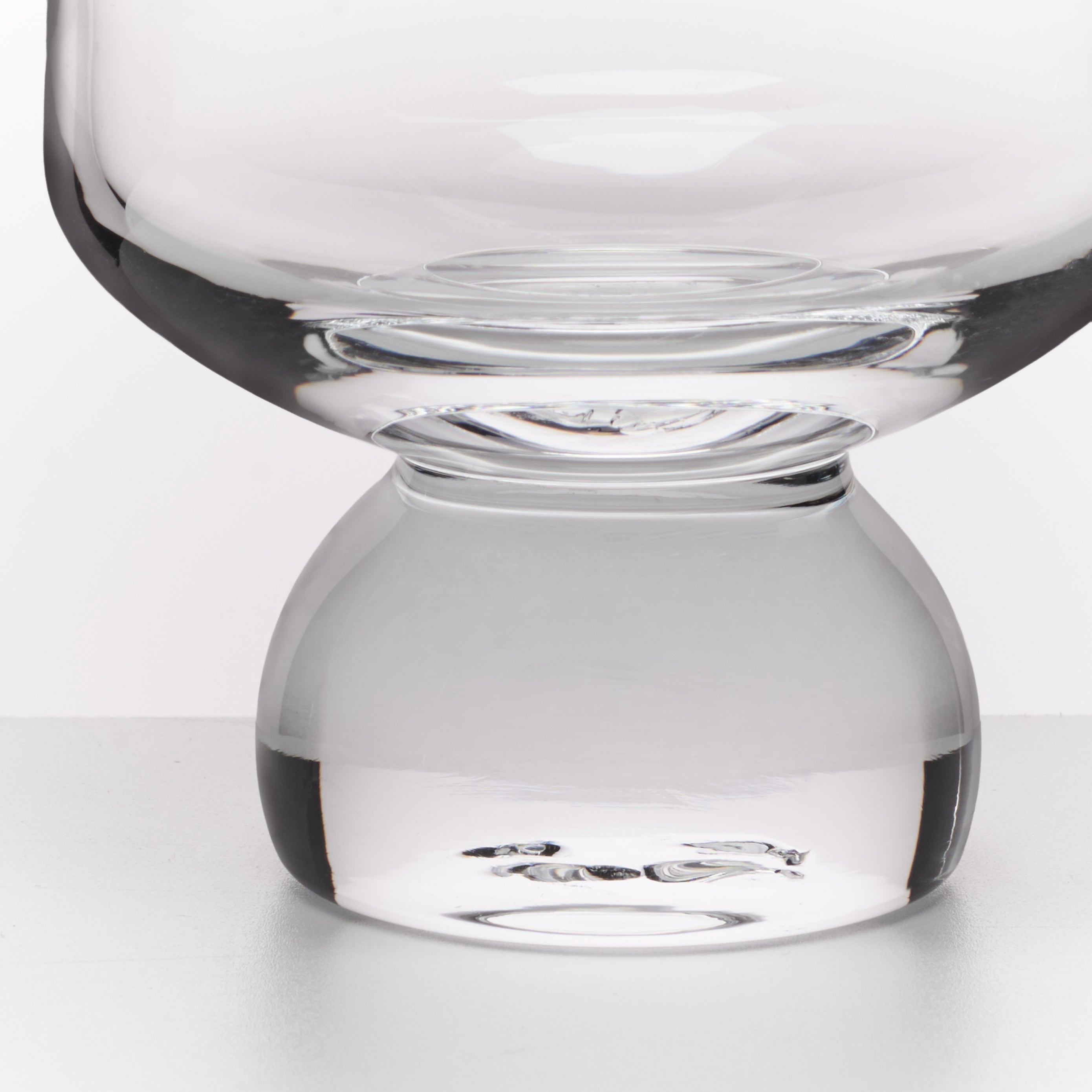 A close-up studio shot of a clear glass vessel with a wide rounded bowl and a thick bulbous base, photographed against a light gray background.