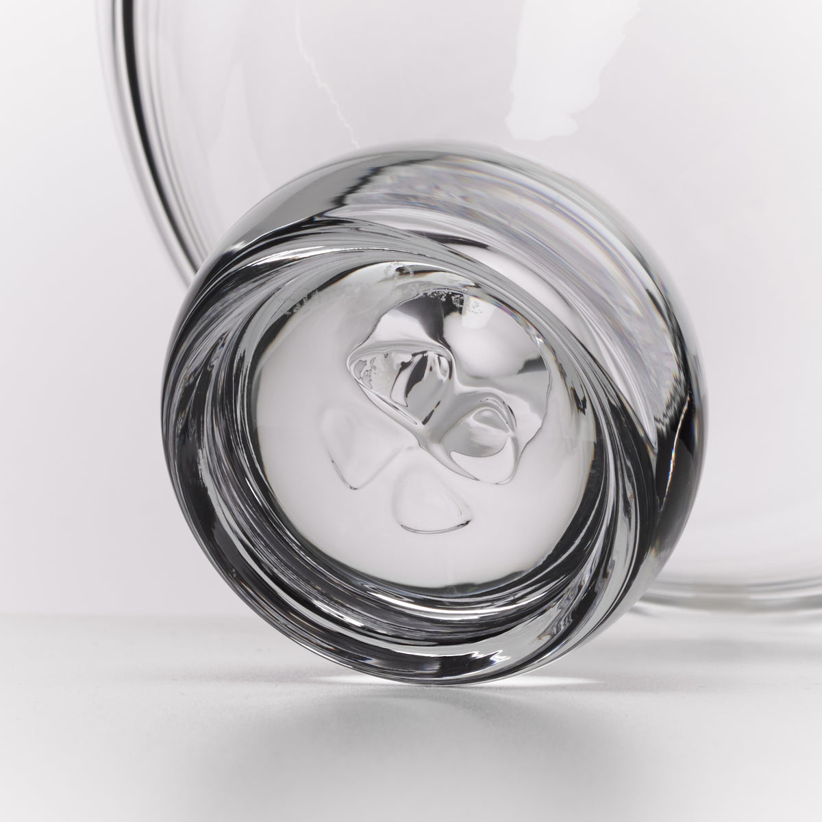 A close-up studio shot of a clear glass tumbler with a thick rim and a sculptural, organic glass base, set against a clean white background.