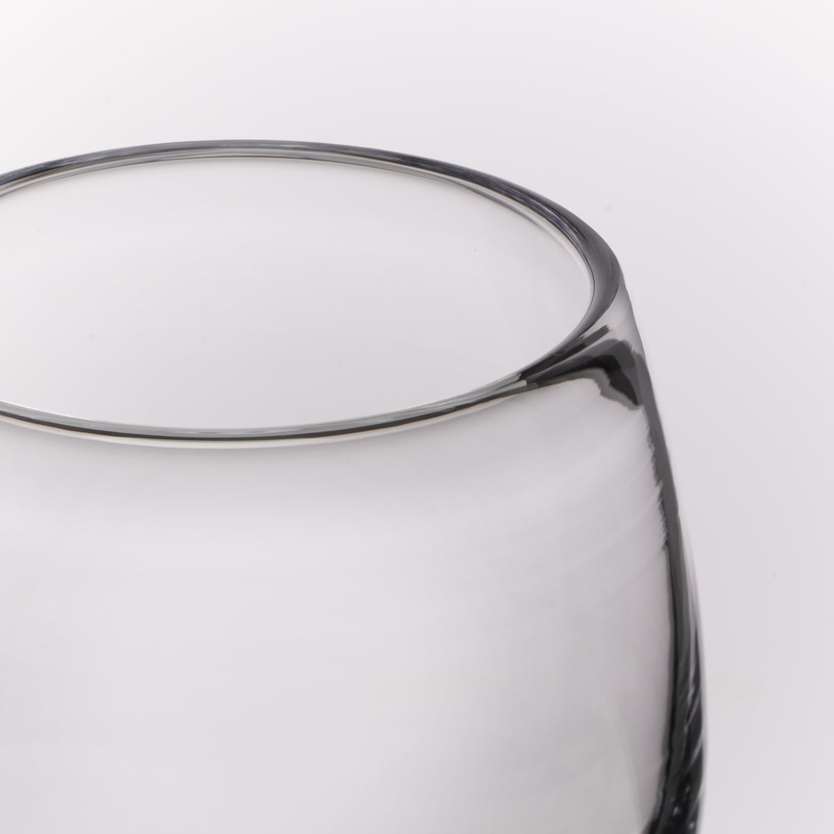Close-up of a clear glass vessel, showing a smooth clear body against a light gray background.