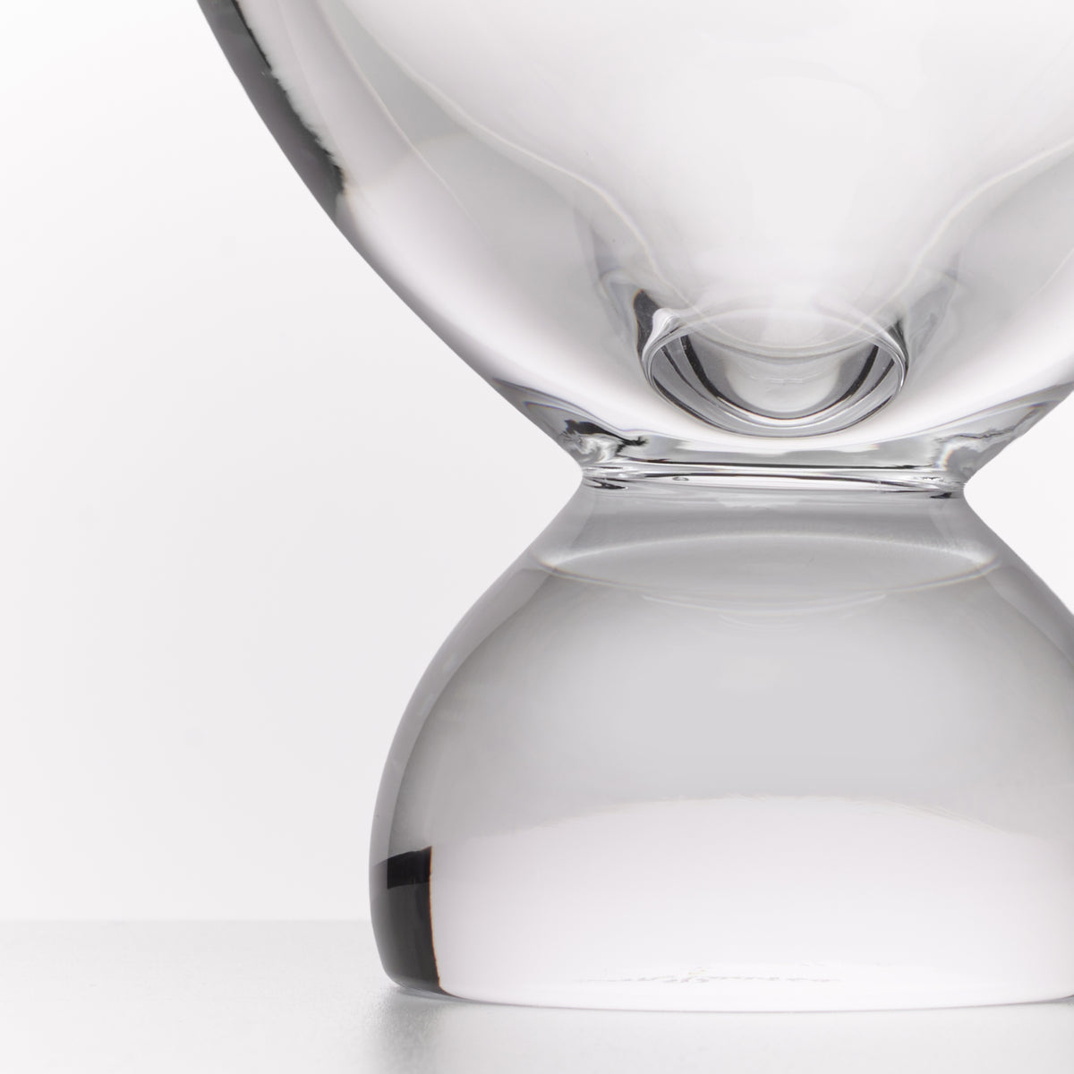 A close-up studio shot of a transparent glass hourglass with a smooth, rounded design on a light gray background.