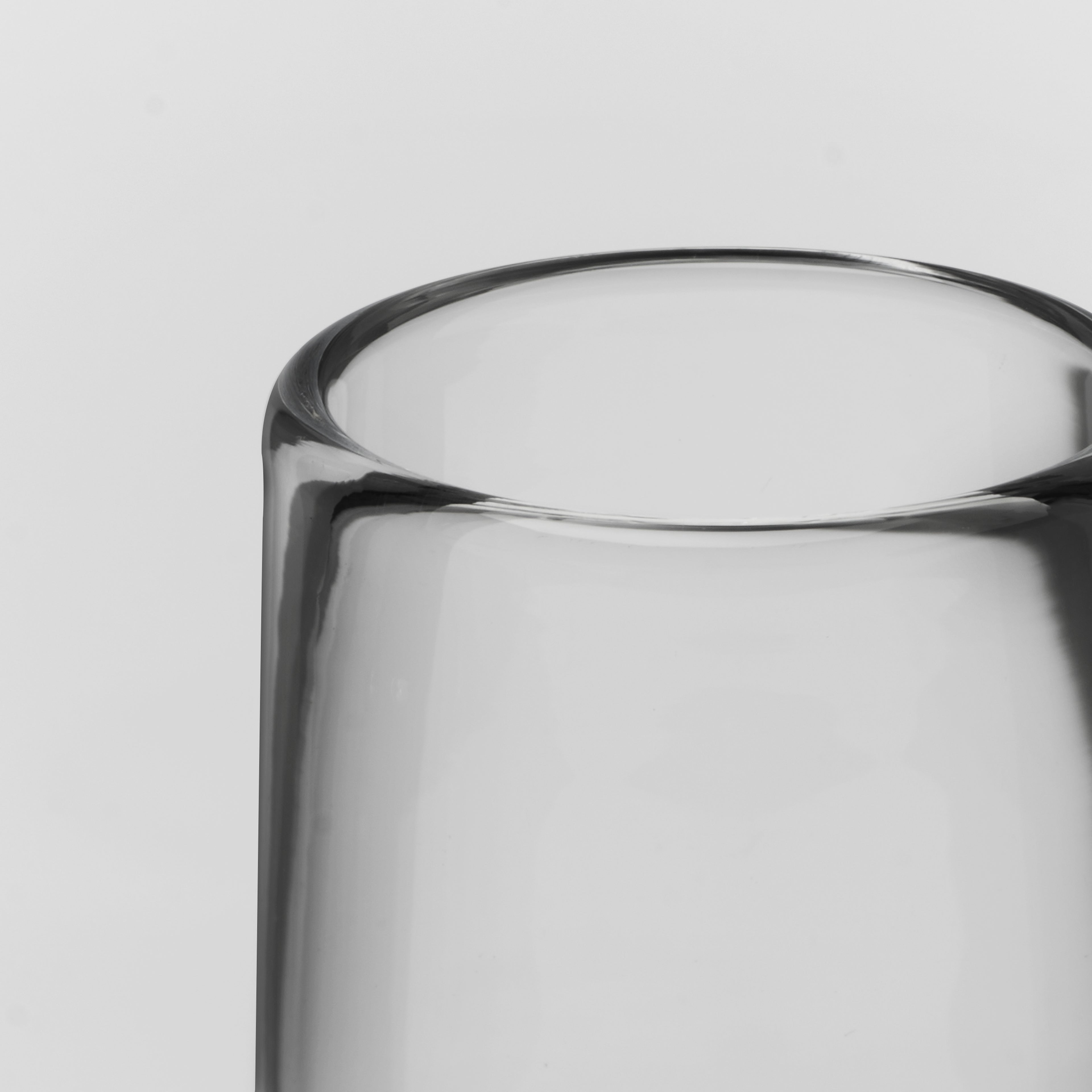 Close-up of a clear glass tumbler or vase showing the top rim and part of the transparent body against a light gray background.