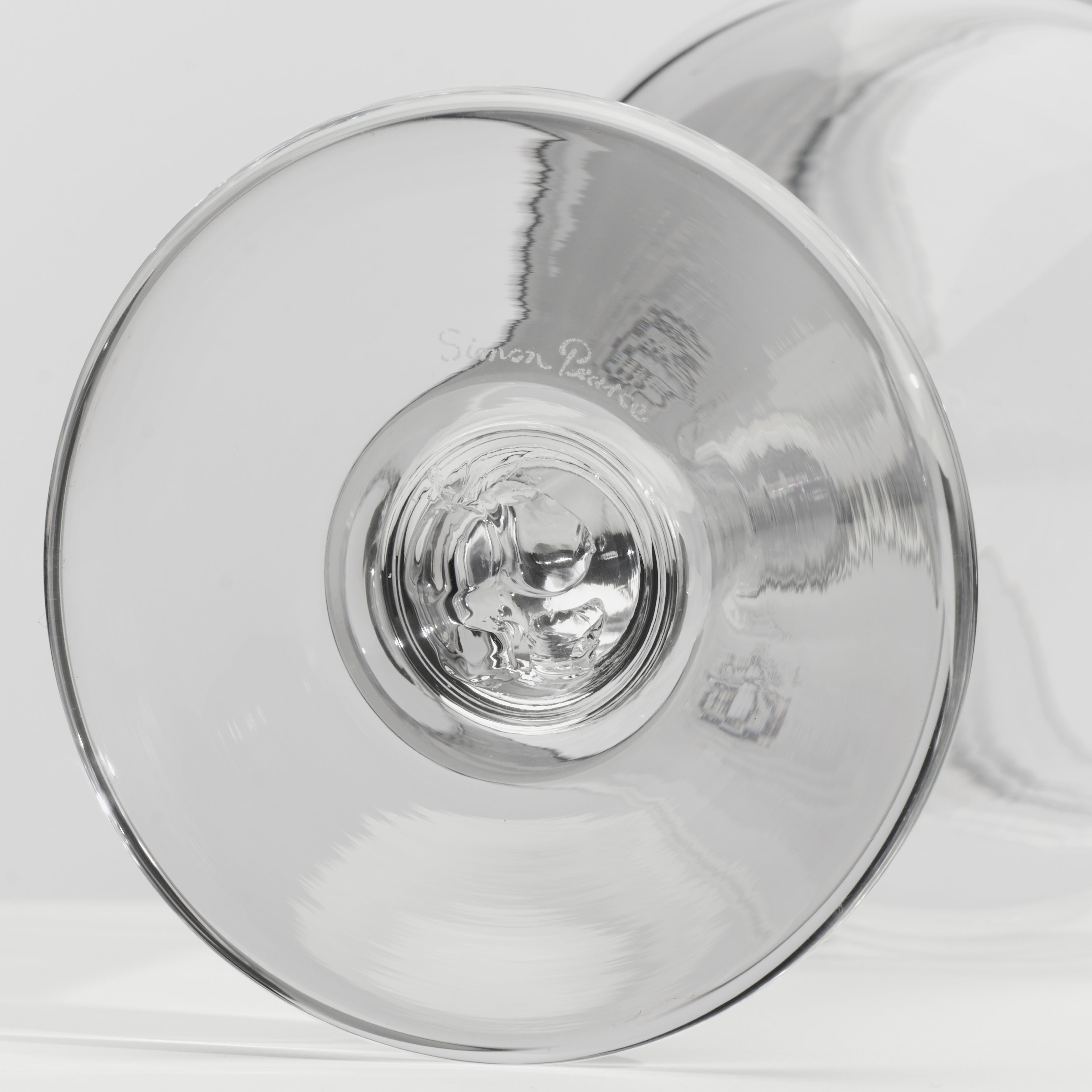 A close-up of a clear glass wine glass viewed from the bottom, showing the circular base and reflections on a light gray background.