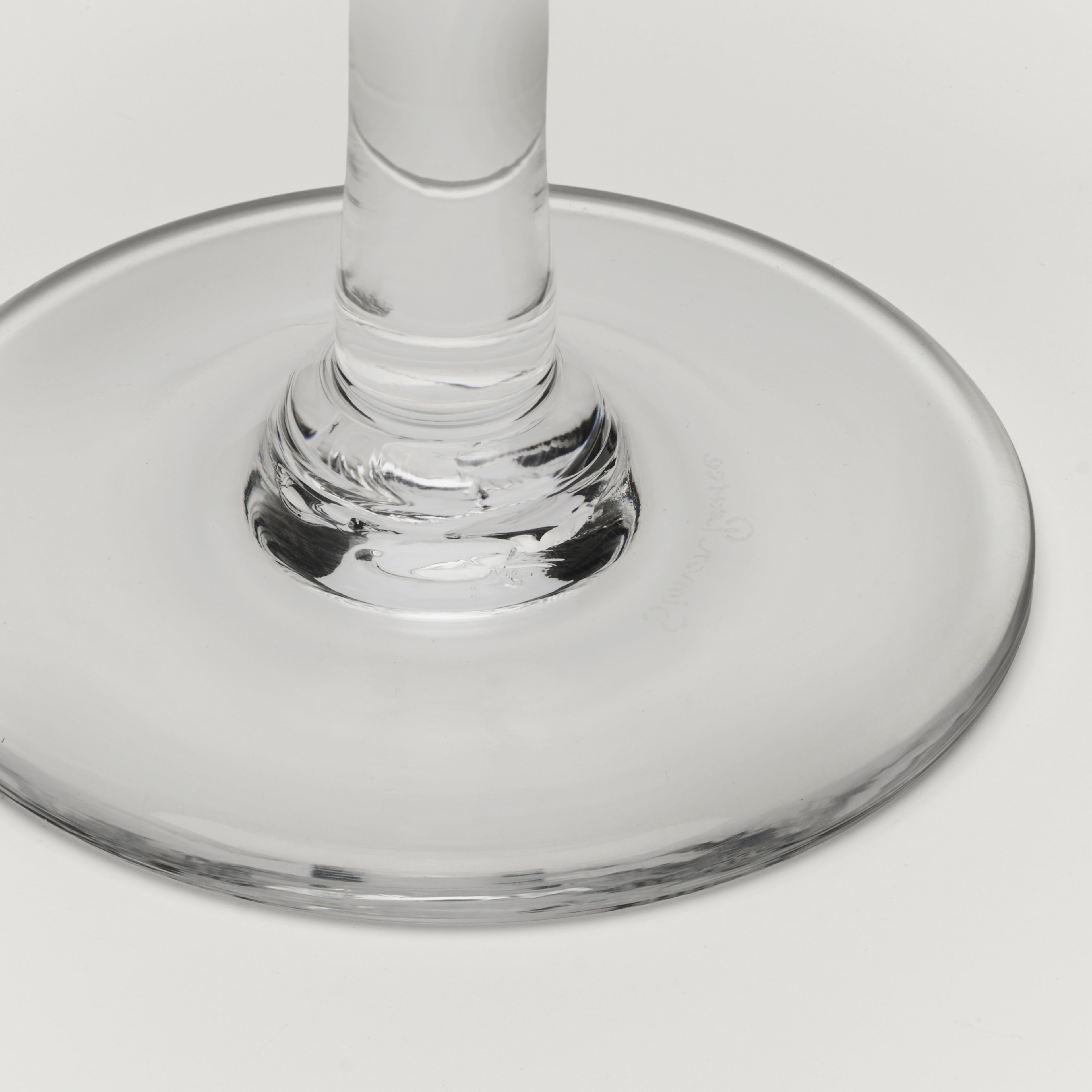 Close-up of a clear glass wine glass base and stem on a light gray background.