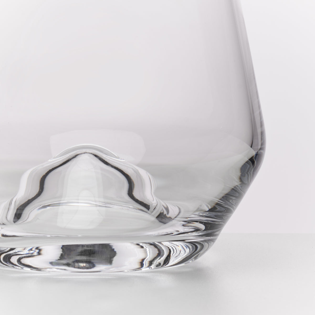 A close-up studio shot of a clear glass with a sculptural, wavy base detail on a clean white background.