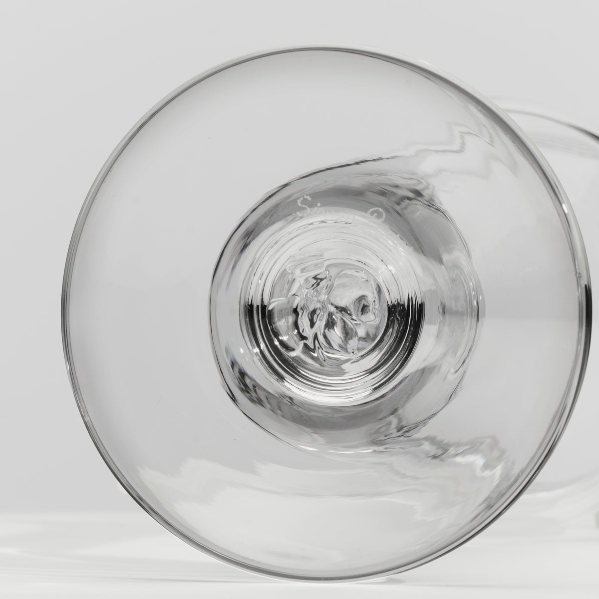 A close-up of a clear glass tumbler, showing the circular base and subtle reflections on a light gray background.