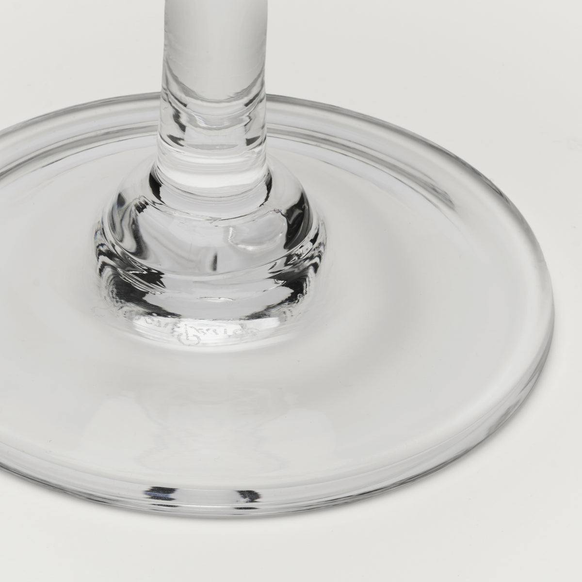Close-up of a clear glass base and stem on a light gray background.