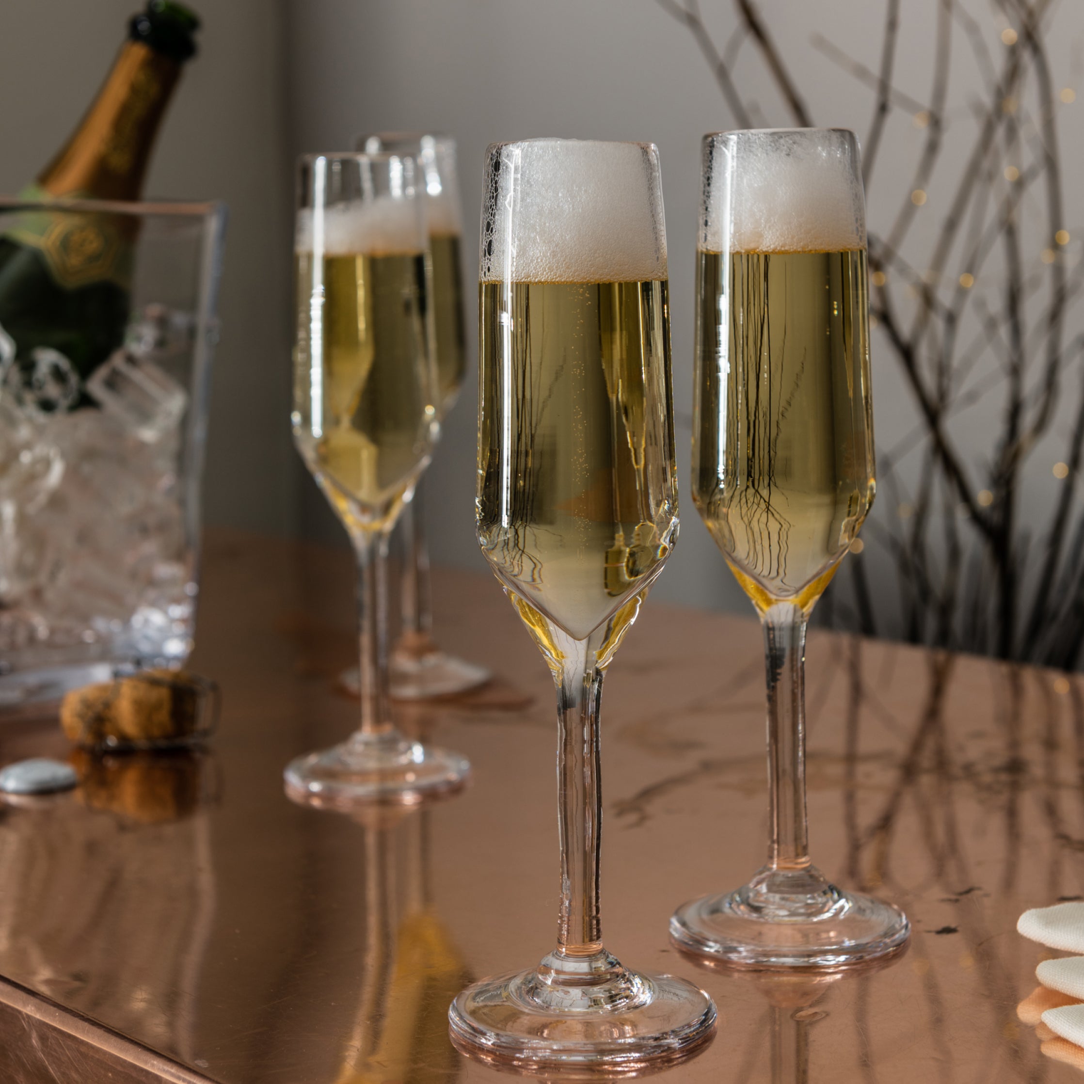 Two champagne flutes filled with sparkling wine on a table with a bottle and cork in the background.