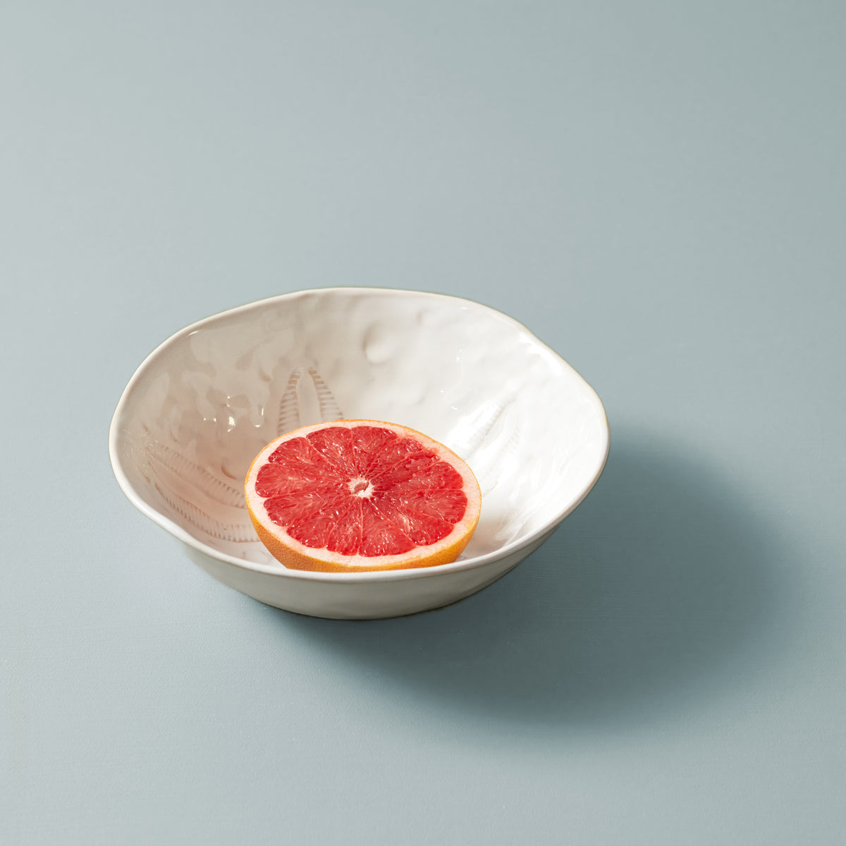 Cream-colored ceramic pasta bowl with embossed sand dollar pattern, containing a grapefruit slice.