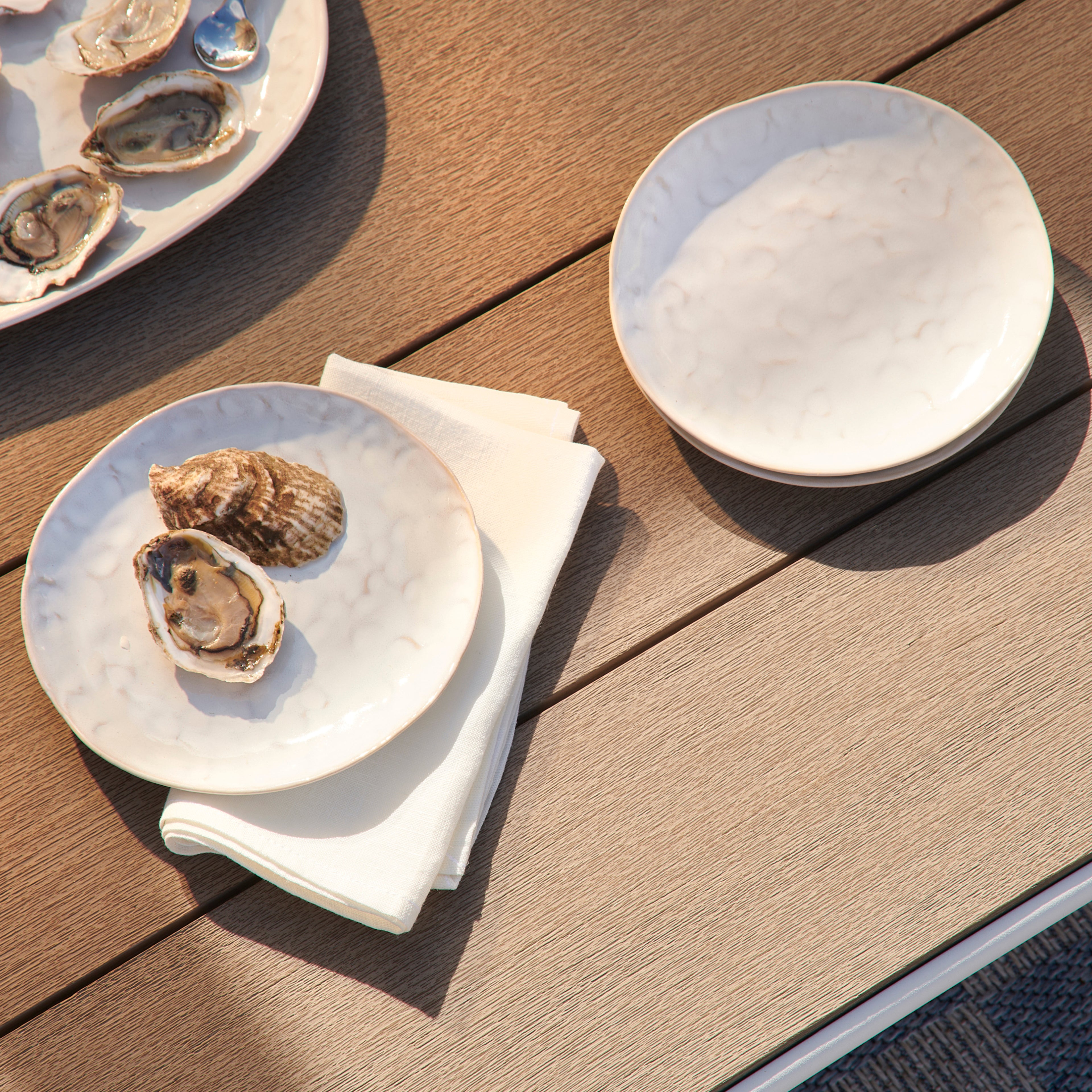 Four white appetizer plates with cloud-shaped rim displayed on wooden table, one holding oysters.