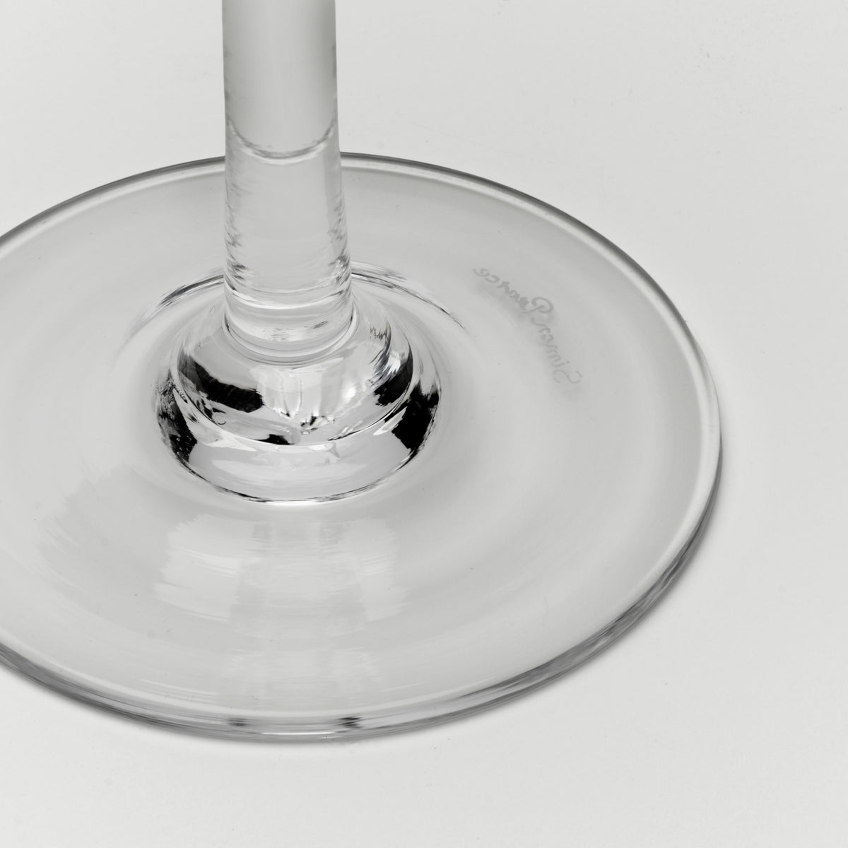 A close-up of a clear glass wine glass base and stem on a light gray background.