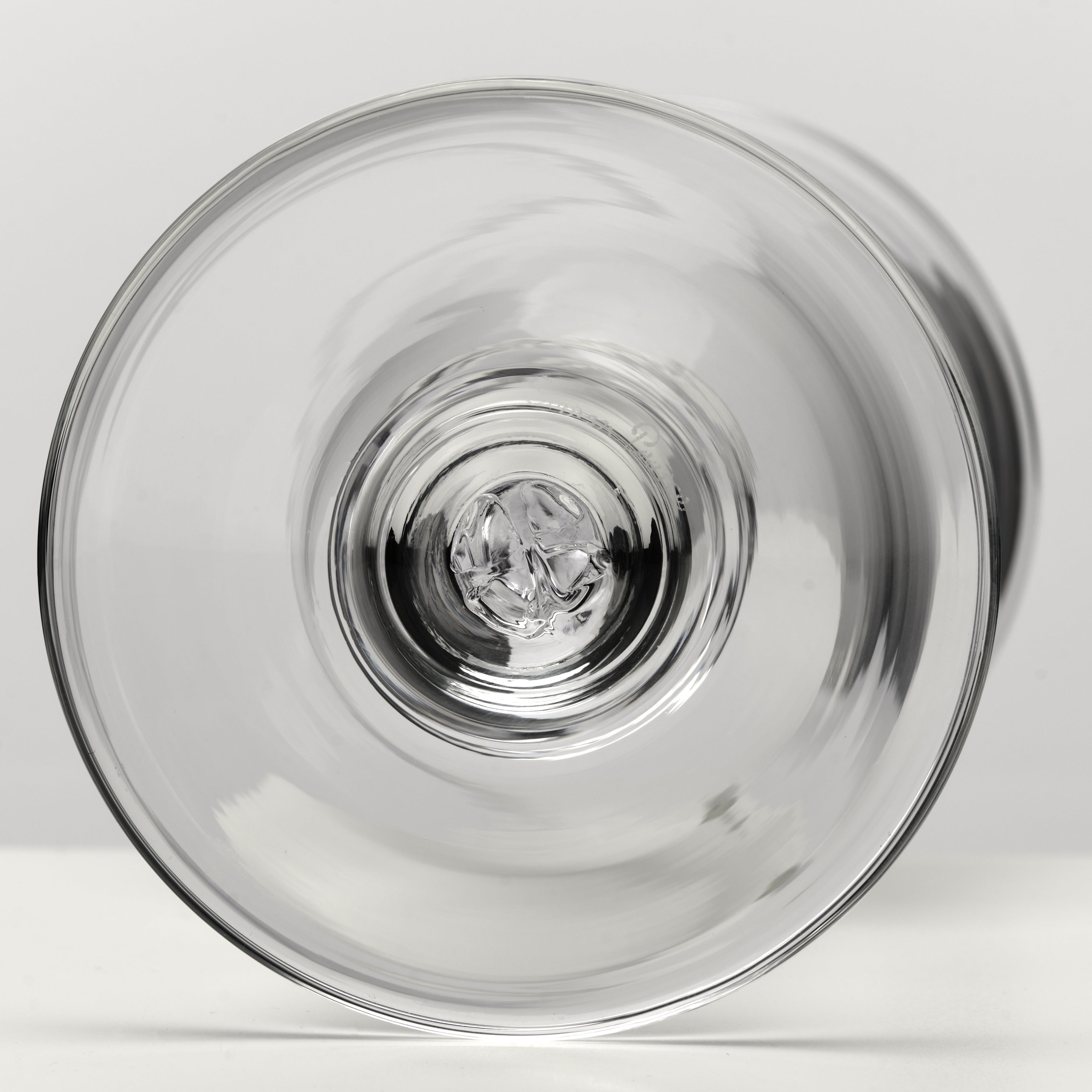 A clear glass stemware glass viewed from the bottom, showing the transparent circular rim and reflective glass center against a light gray background.