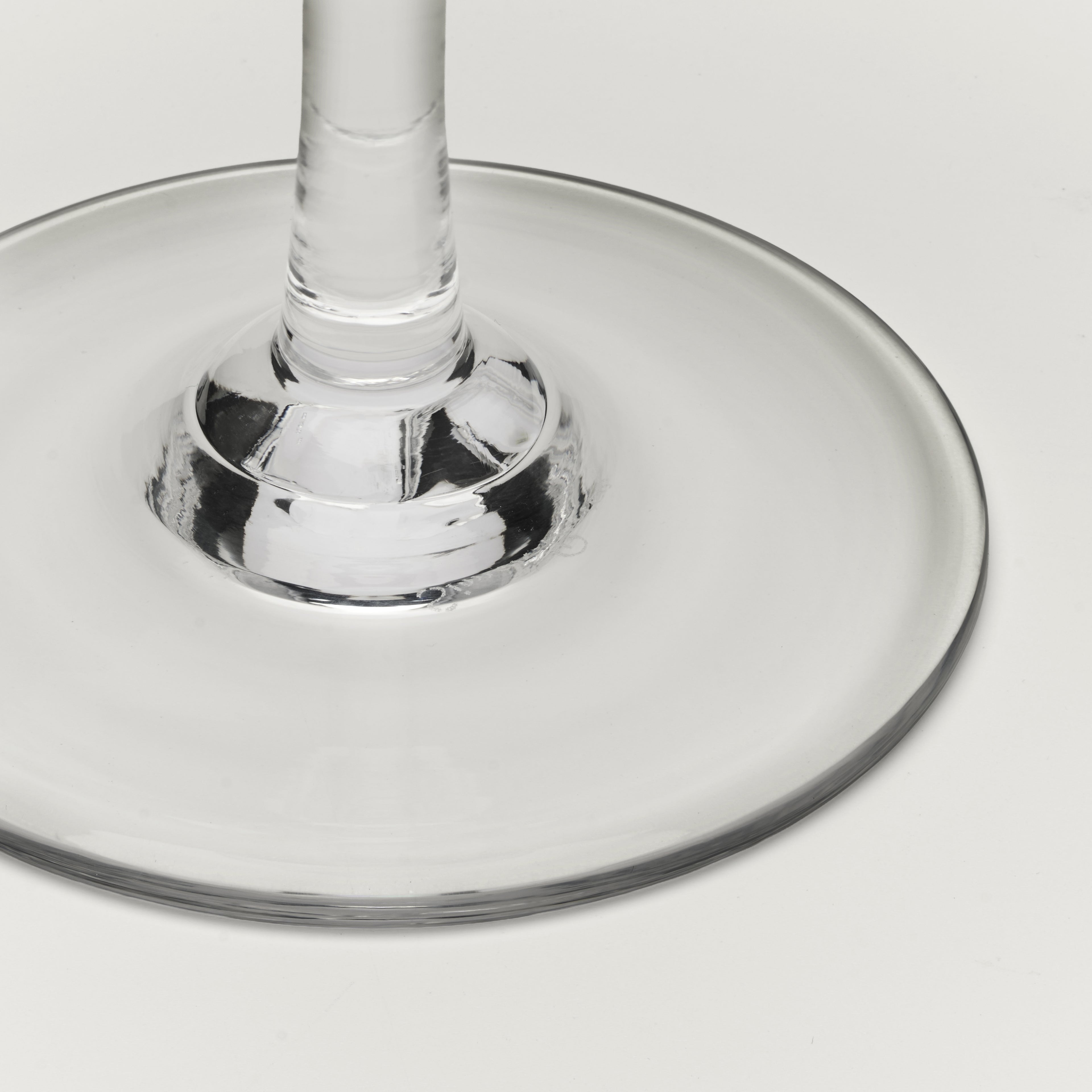 Close-up of a clear glass wine glass base and stem on a light gray background.