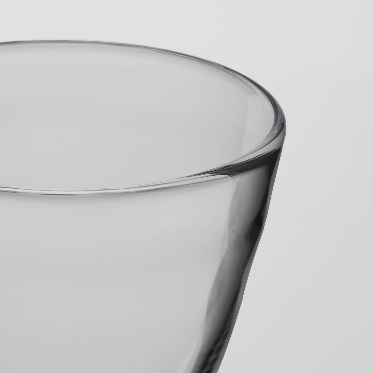 Close-up of a transparent drinking glass with a thick, slightly flared rim, shown against a light gray background.