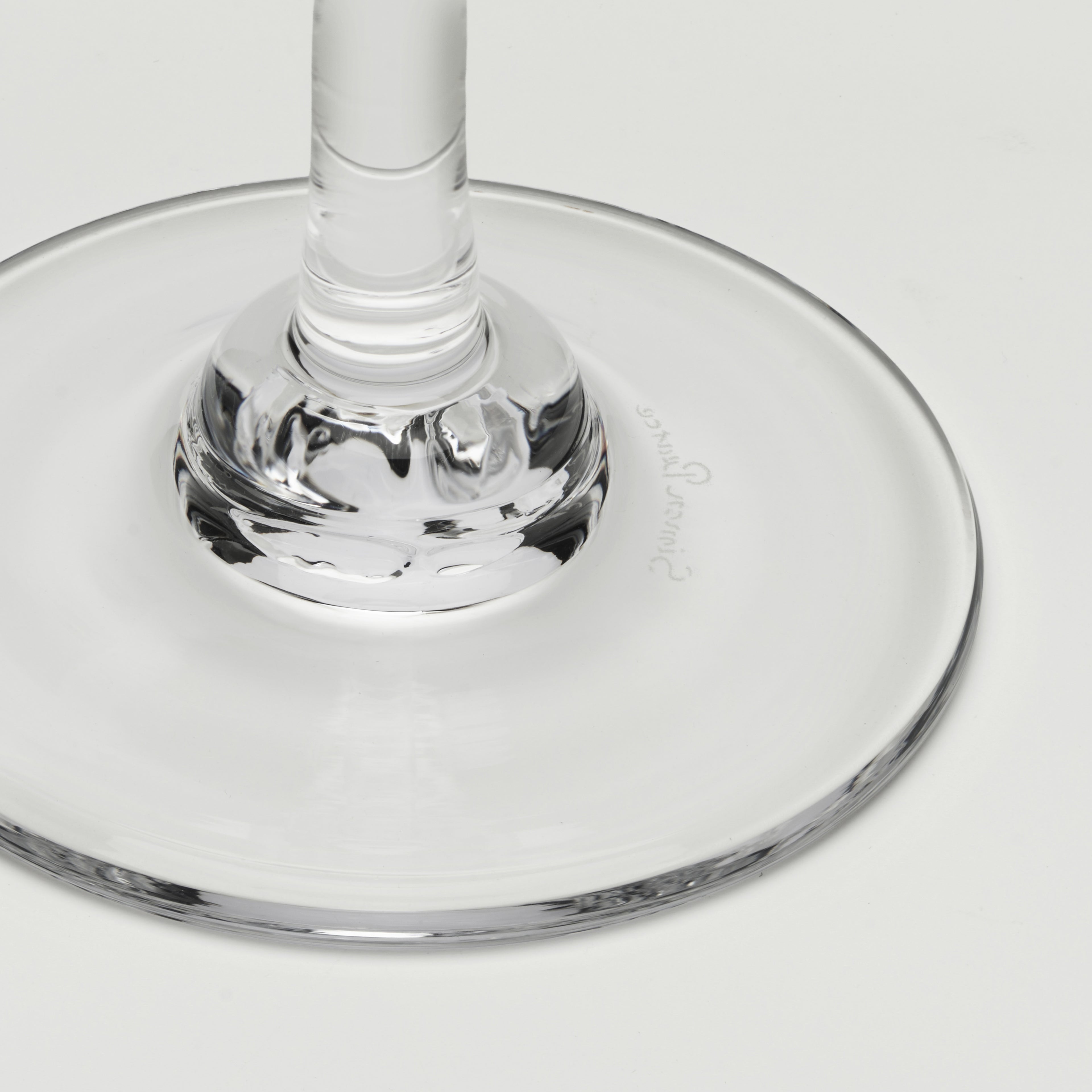 Close-up of a clear glass wine glass base and stem on a light gray background.