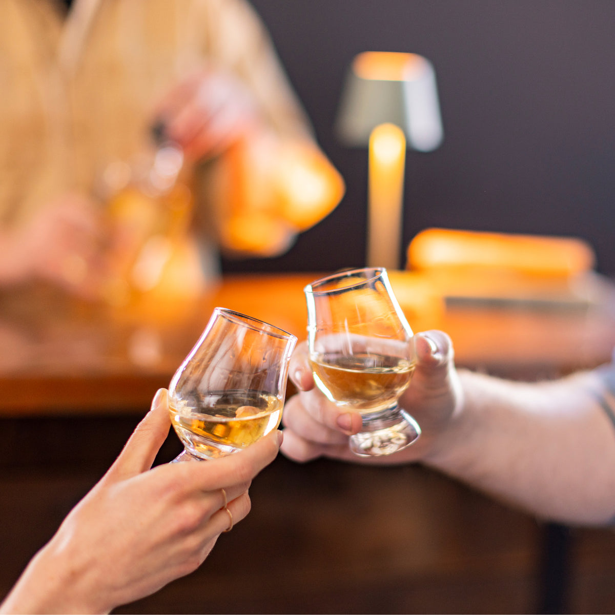 Two clear glasses filled with amber-colored liquor being held up in a toast.