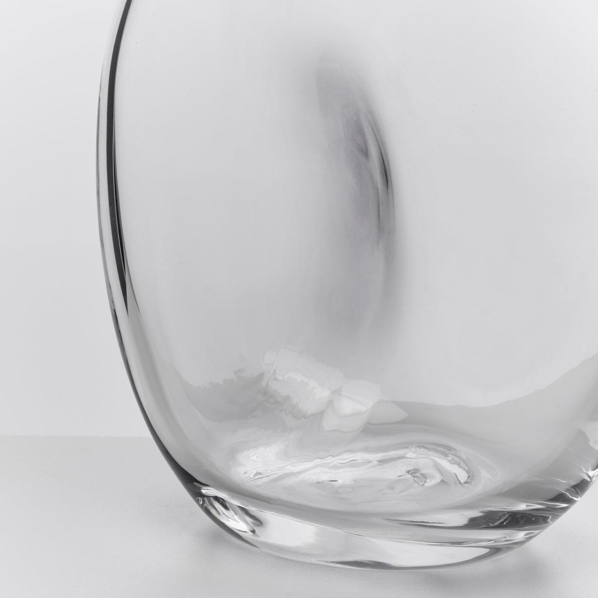 Clear glass carafe with curved, organic shape and dark rim, shown from side angle against white background.