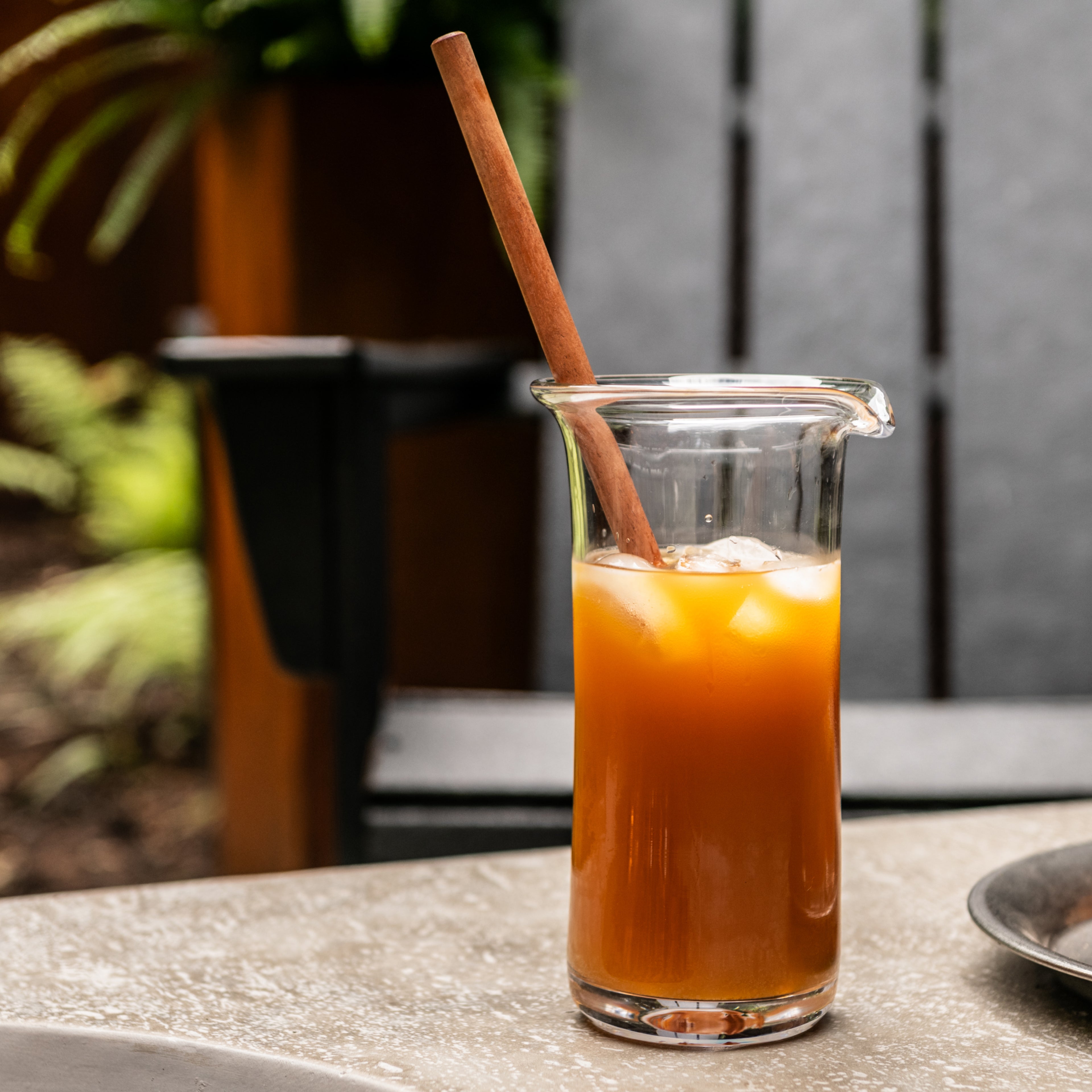 Brown wooden cocktail stirrer in a glass pitcher filled with amber liquid and ice.