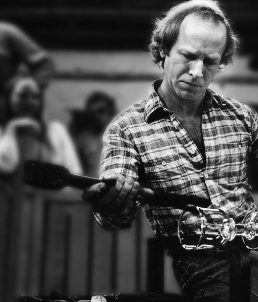 Black and white photograph of Simon Pearce shaping molten glass with a wooden paddle in his studio