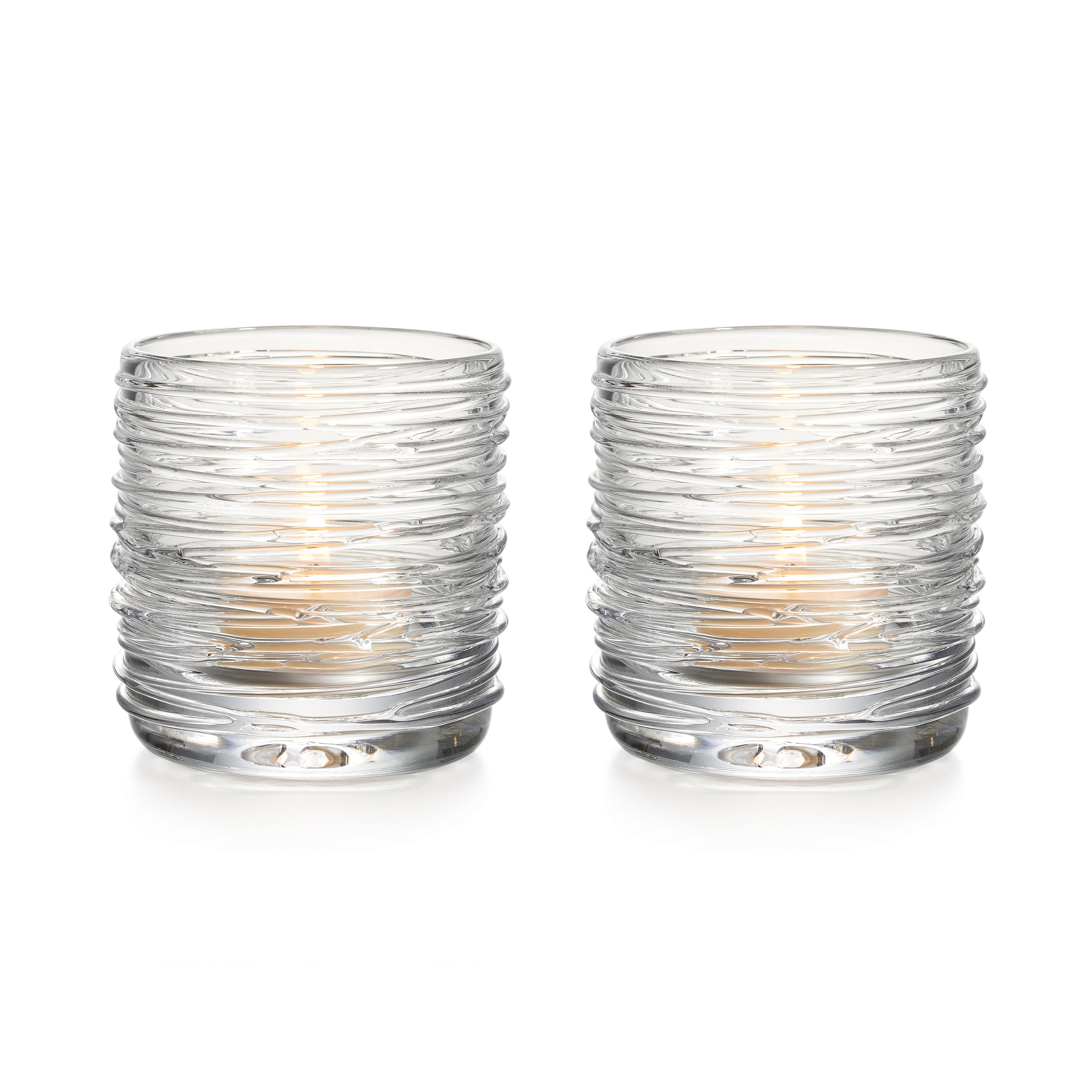Two clear glass tealight holders with textured horizontal ridges and lit candles inside.