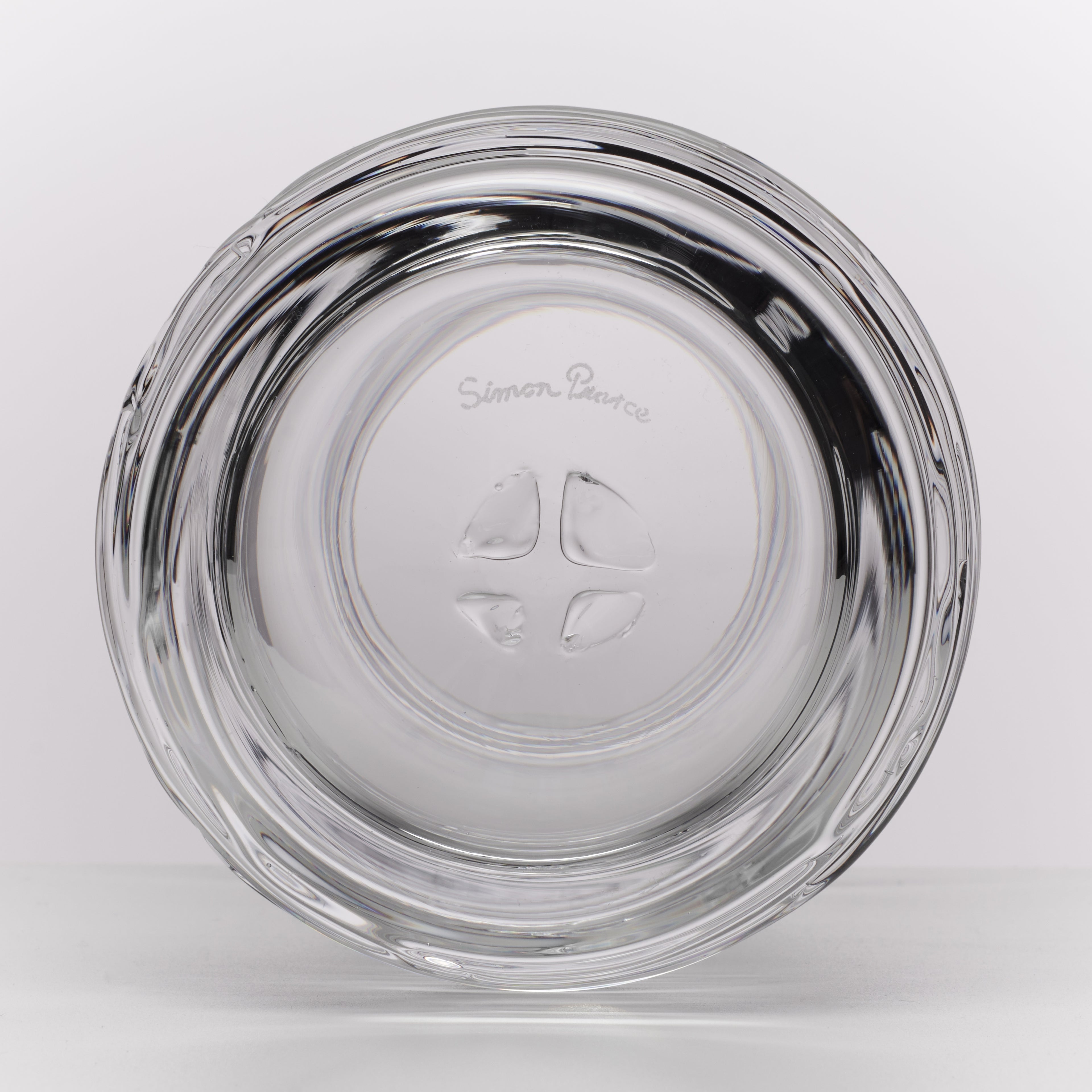 A clear glass ashtray with a flared rim and embossed brand name 'Simon Pearce' in the center, shown on a light gray background.