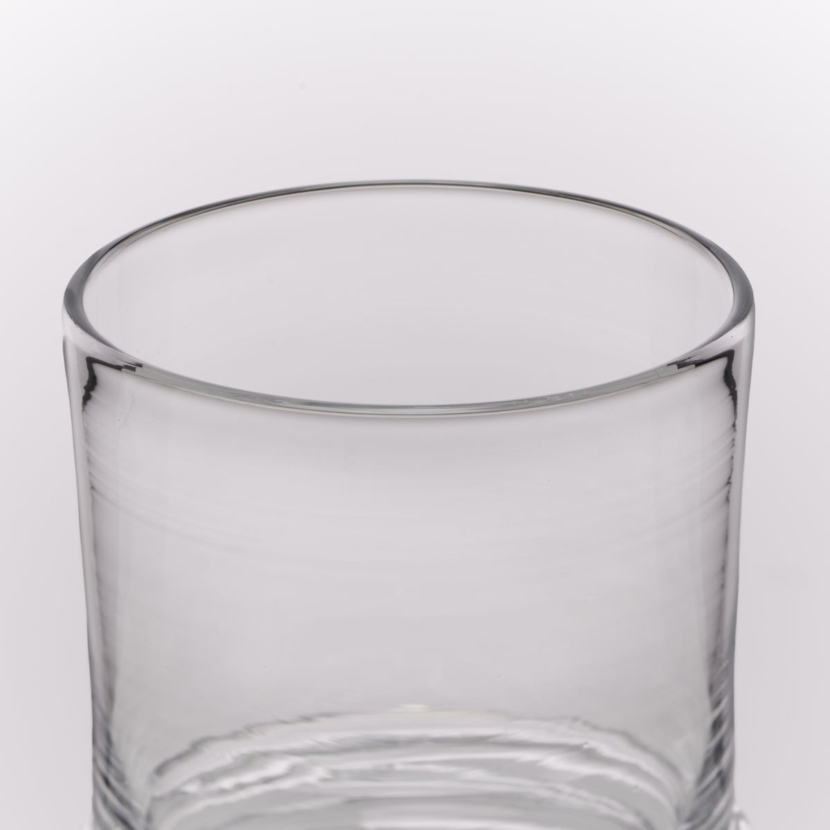 A clear glass tumbler with a thick rim and subtle horizontal ridges near the base, shown on a clean white background.